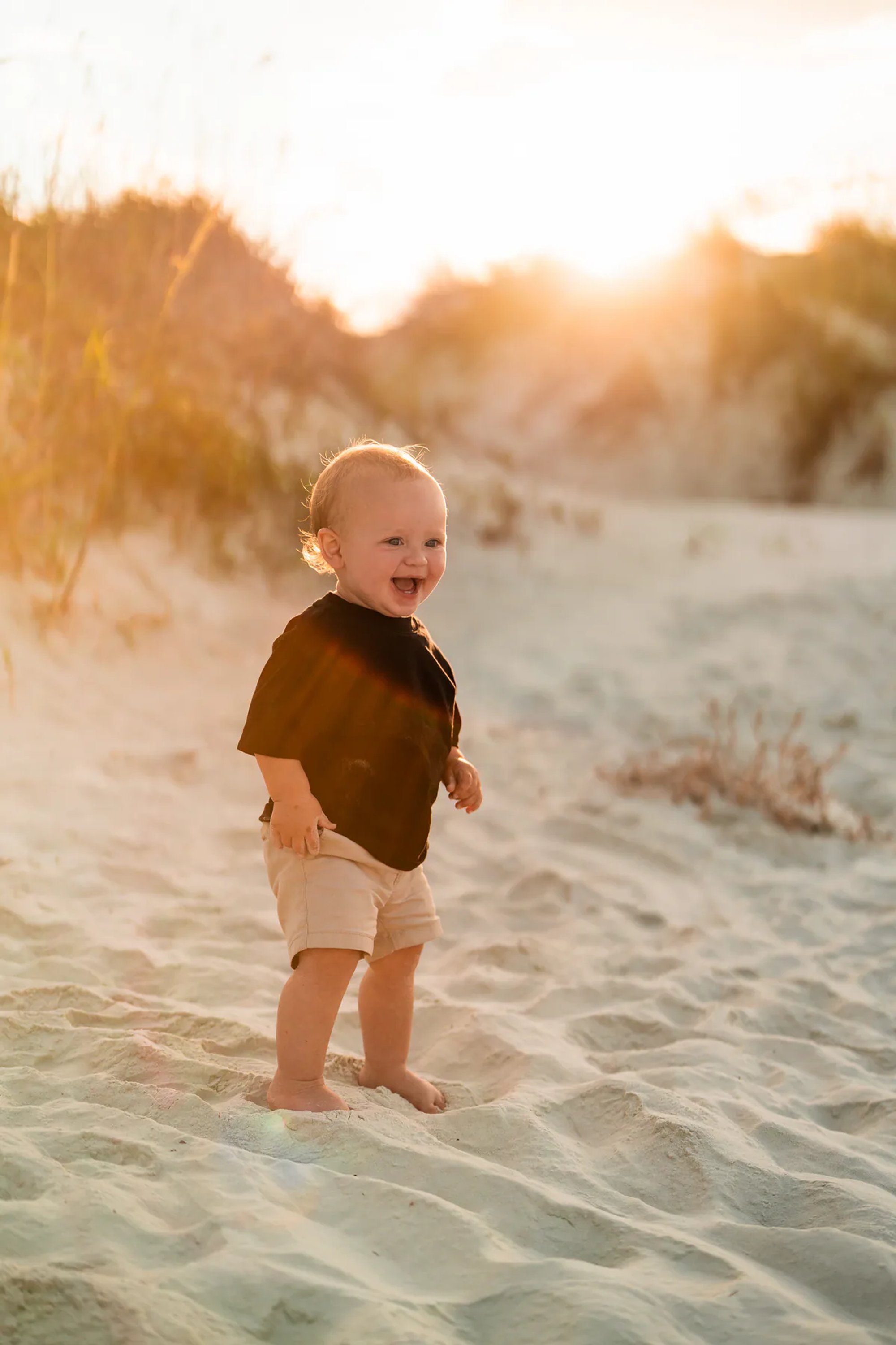Toddler smiling in the sand during a sunset beach photo session at Ponce Inlet Jetty Beach.