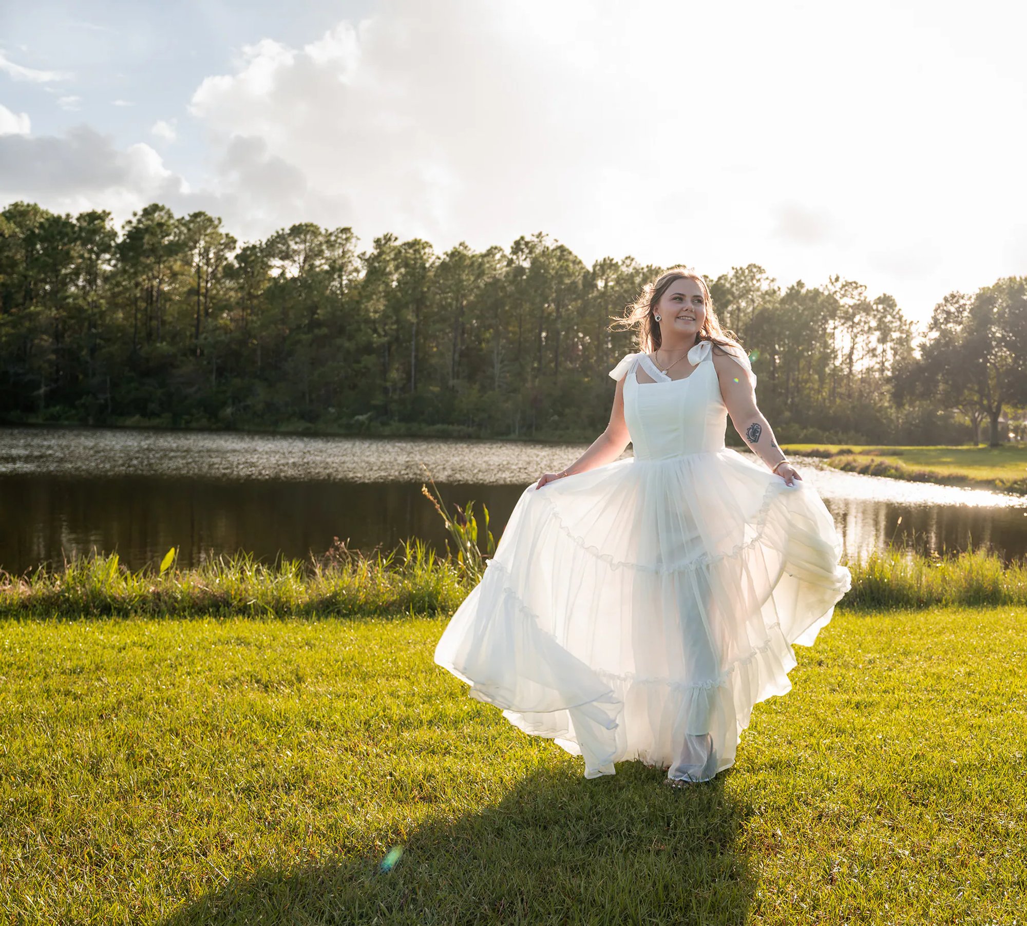 Bride lifting the skirt of her wedding dress on a grassy lakeside lawn.