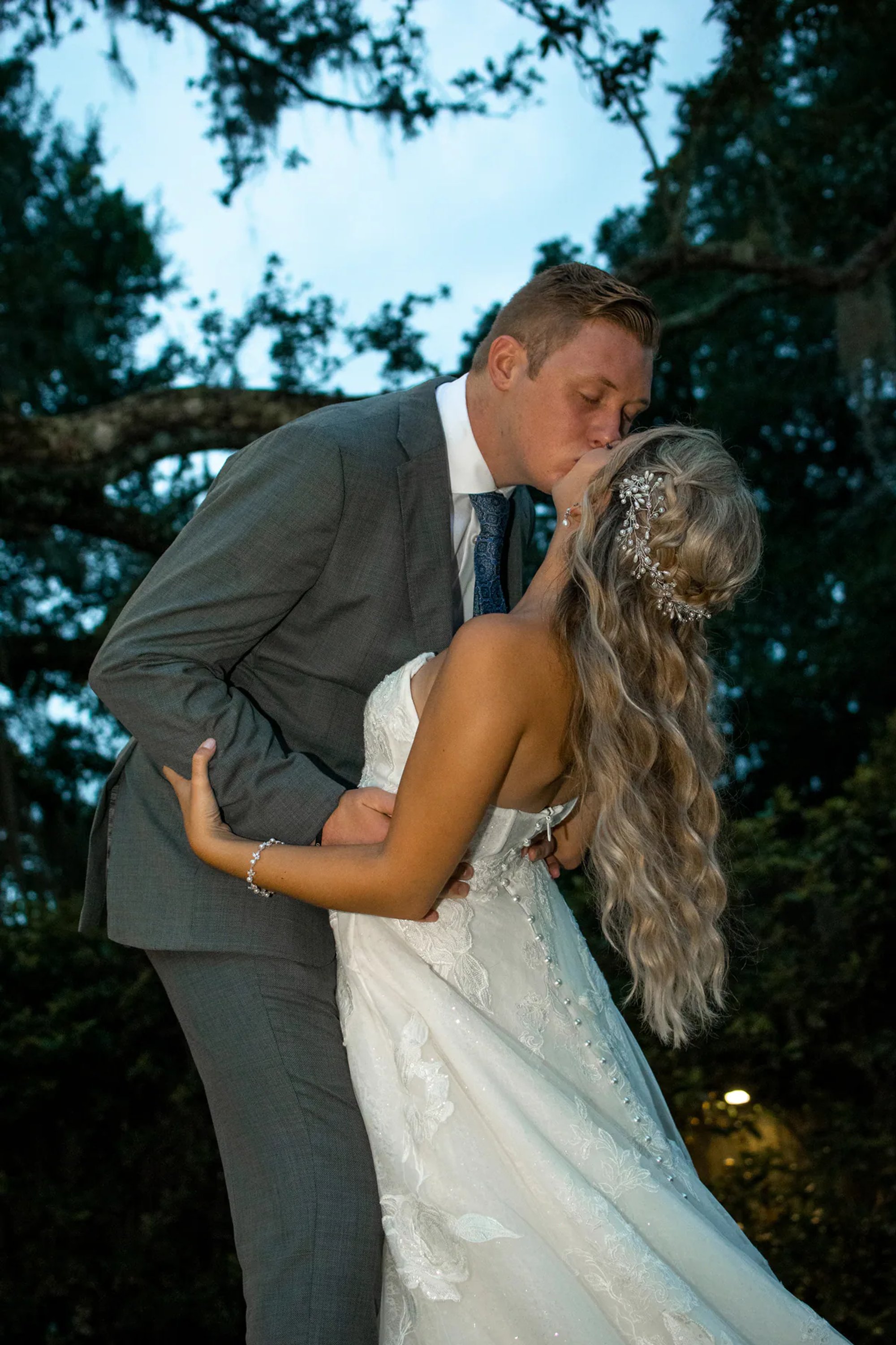 Groom dipping the bride for a kiss beneath the trees.