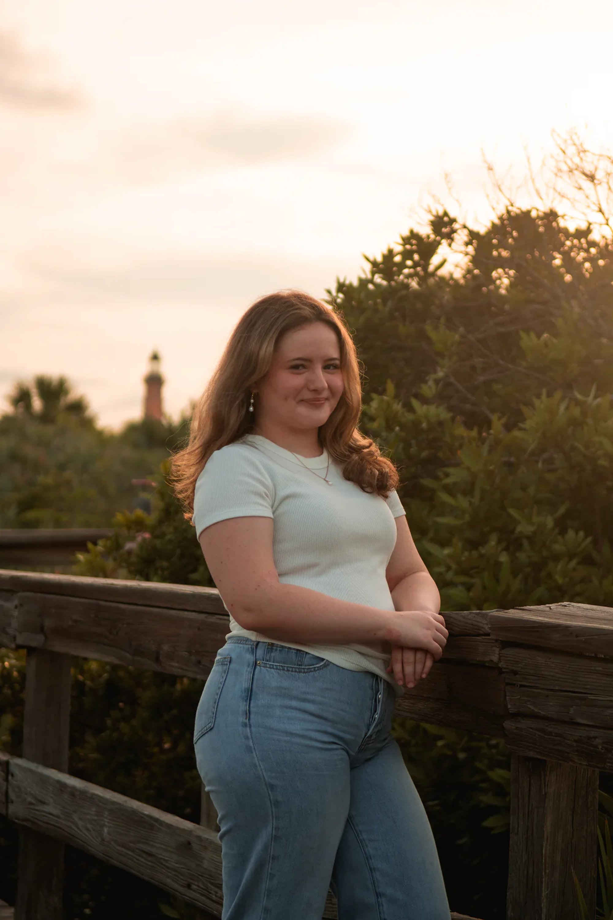 Senior photo at Ponce Inlet FL, Nelly smiling on the boardwalk in jeans and white top with sunset glow.