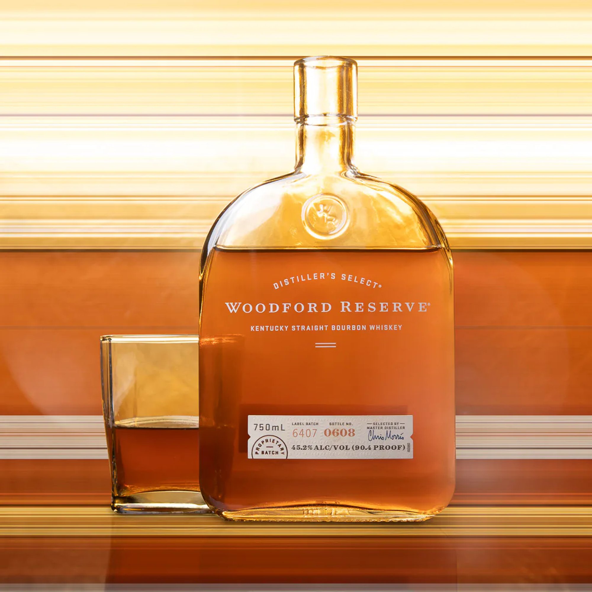 Woodford Reserve bourbon bottle and tumbler against a layered amber backdrop.