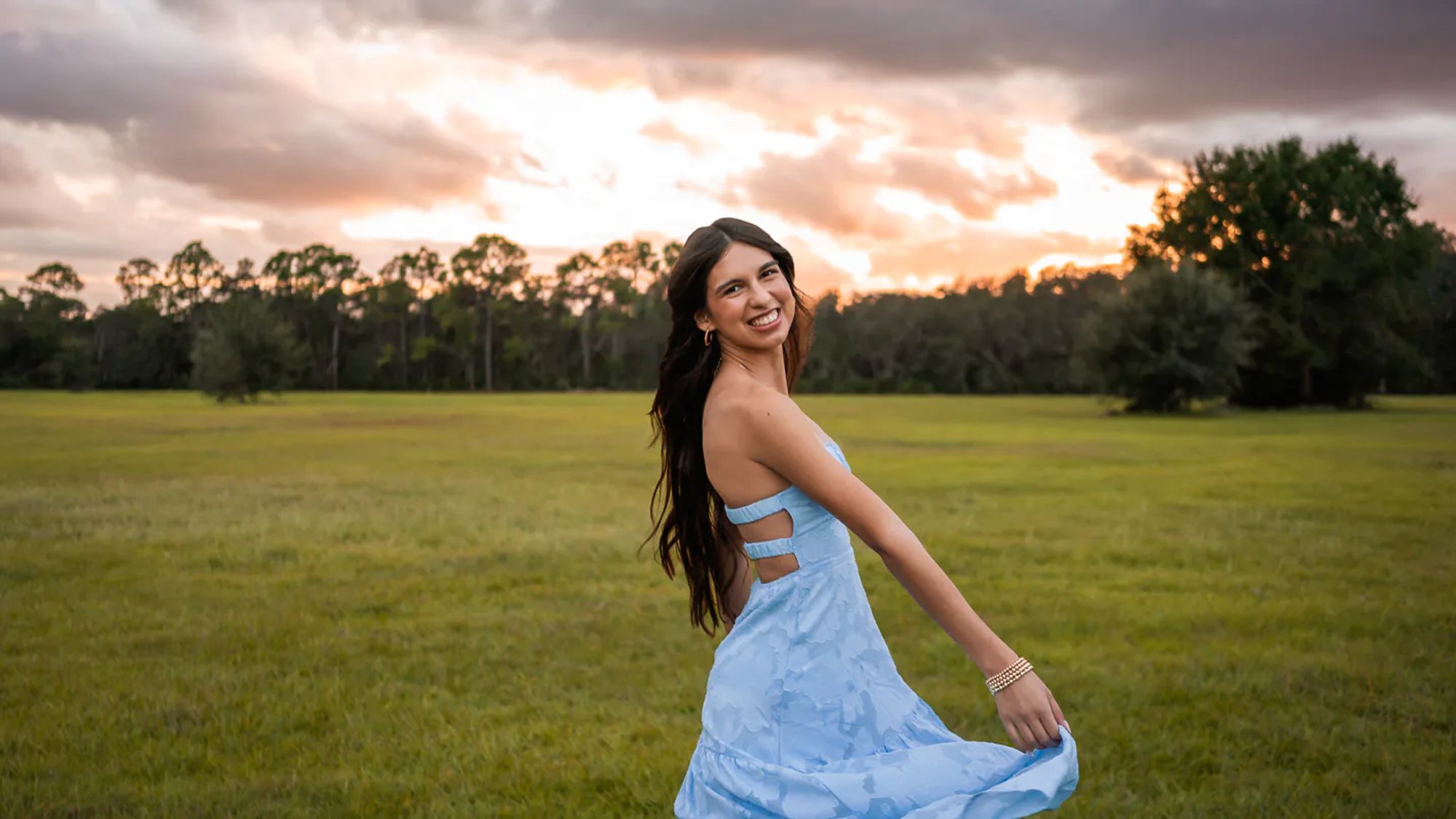 Young woman twirling a pale blue dress across an open field.