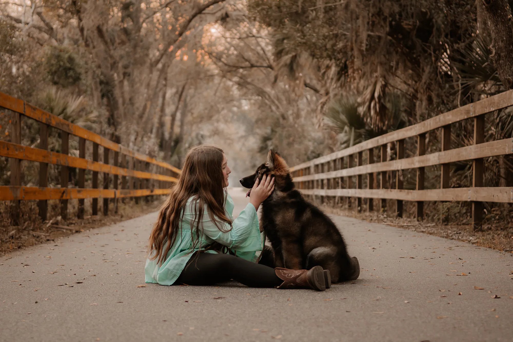 Young woman gently holding her black dog's face while seated on a road.