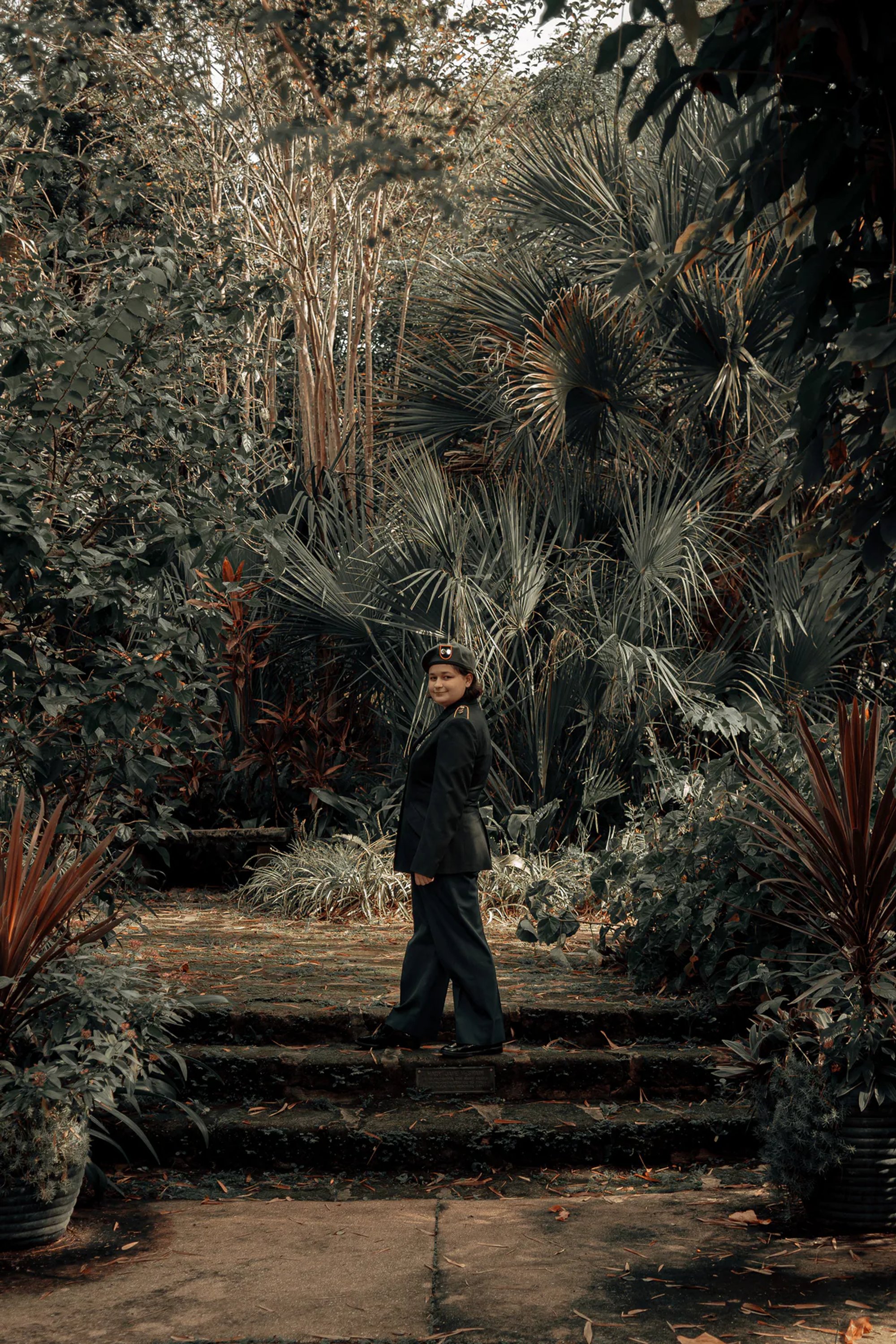 Person in dark clothing standing among dense tropical plants.
