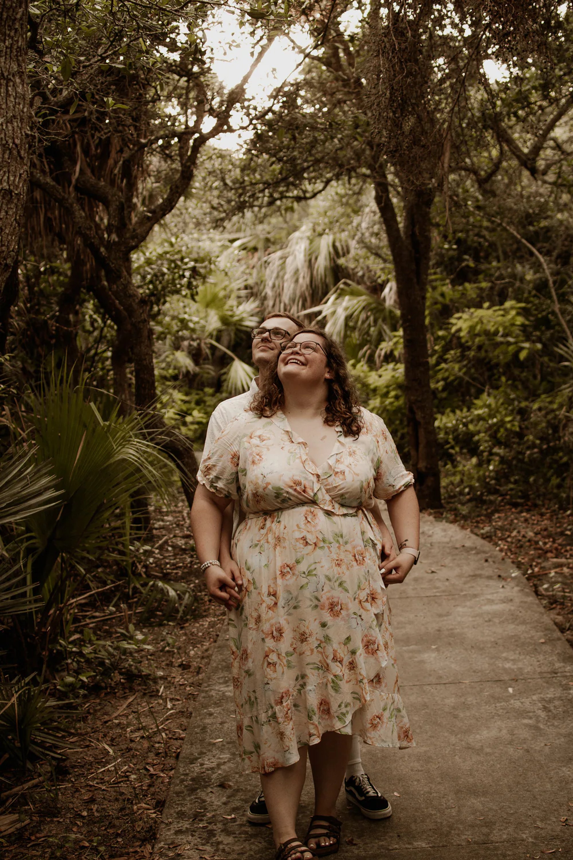 Woman in a floral dress walking along a wooded path.