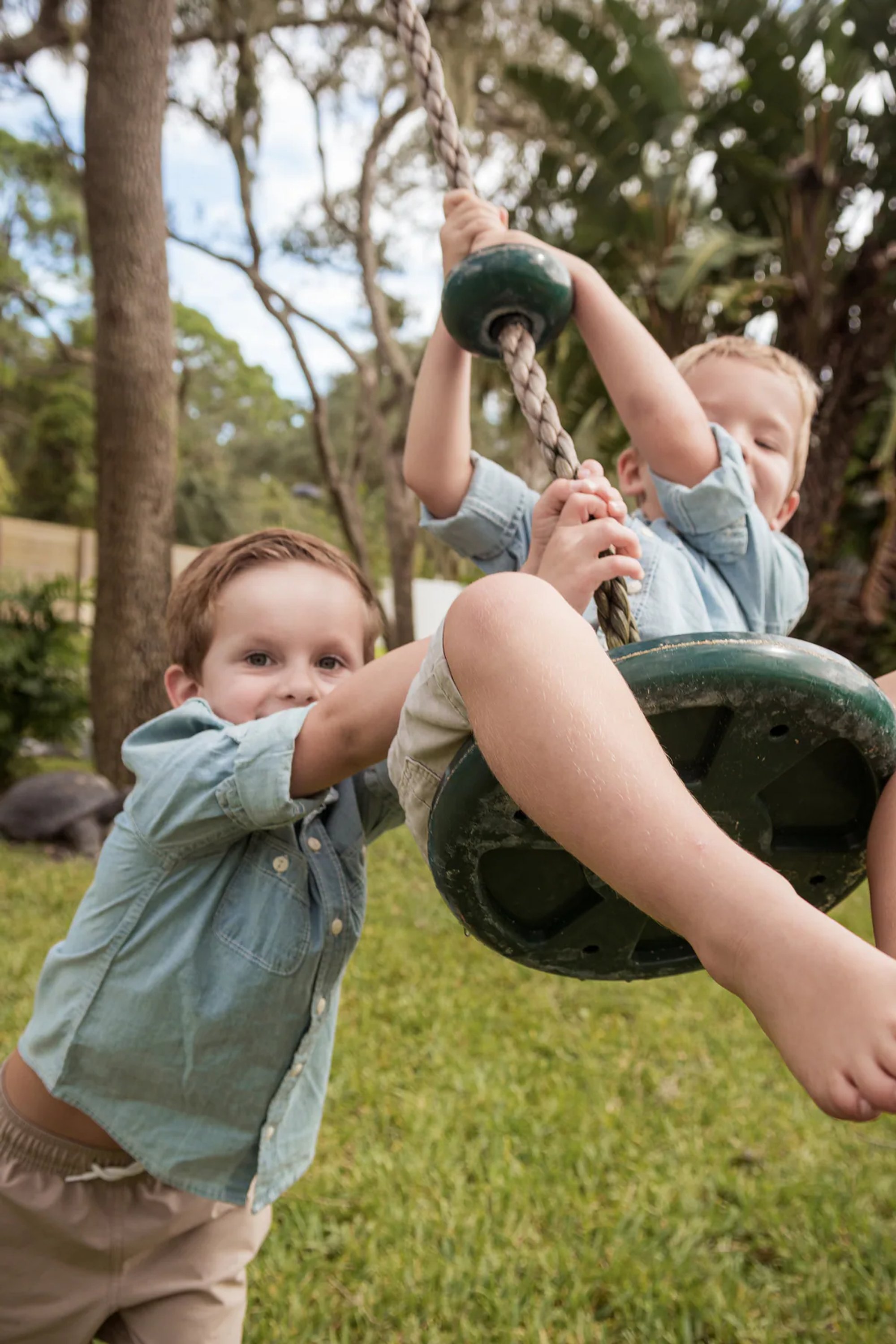 Young child pushing another child on a tire swing.