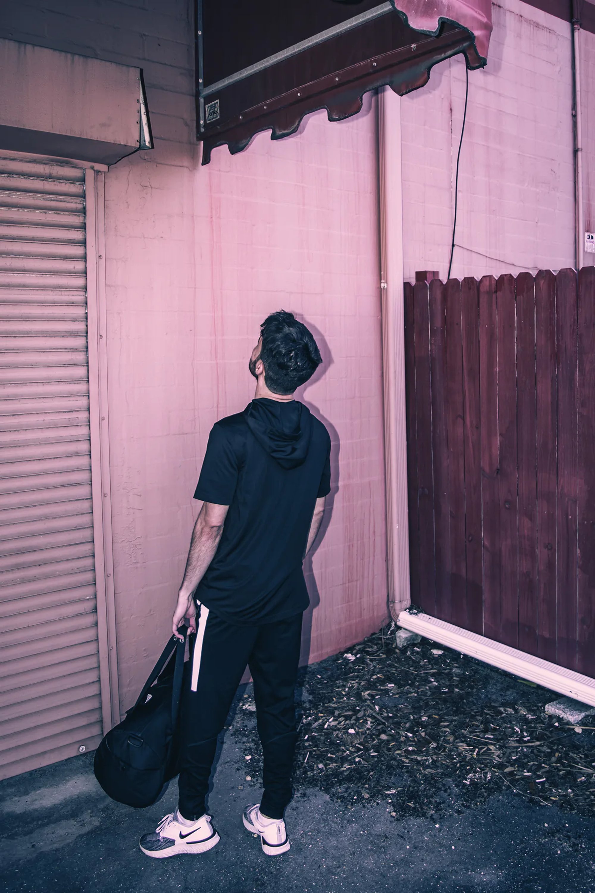 Person carrying a cap and bag beside a pink industrial wall.
