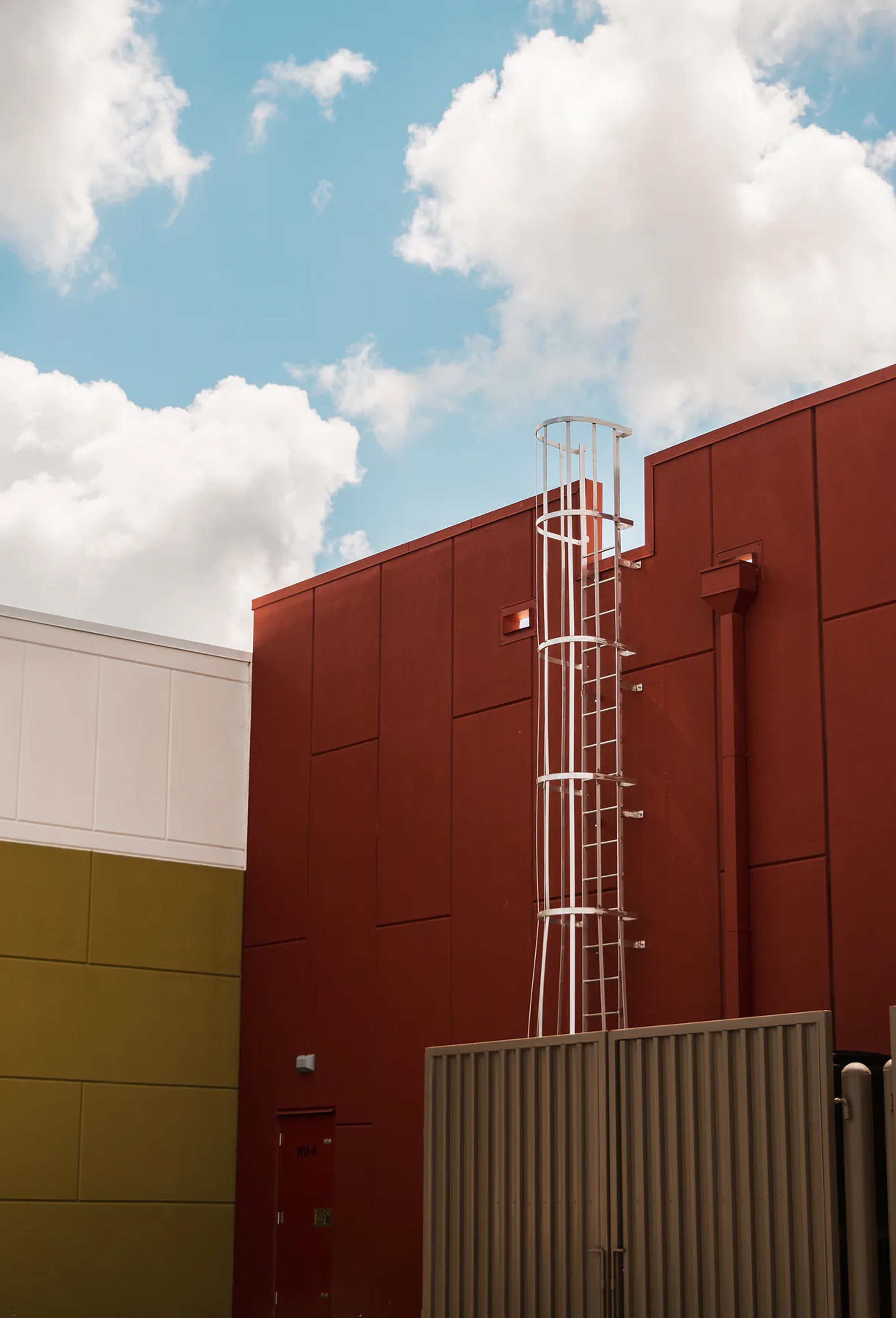 Red and yellow industrial building walls with an exterior metal ladder.