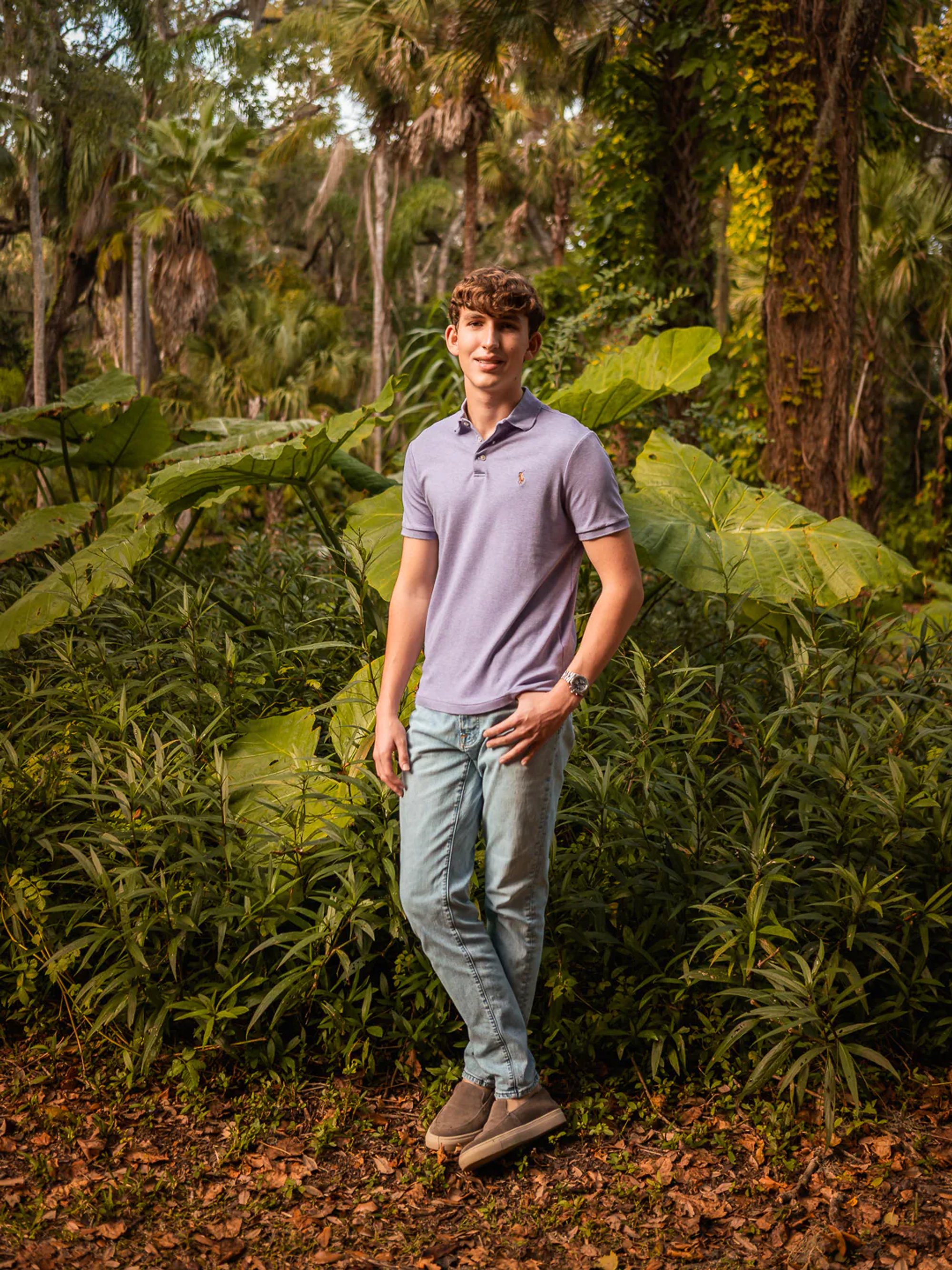 Full-length senior portrait of a young man among tropical plants.