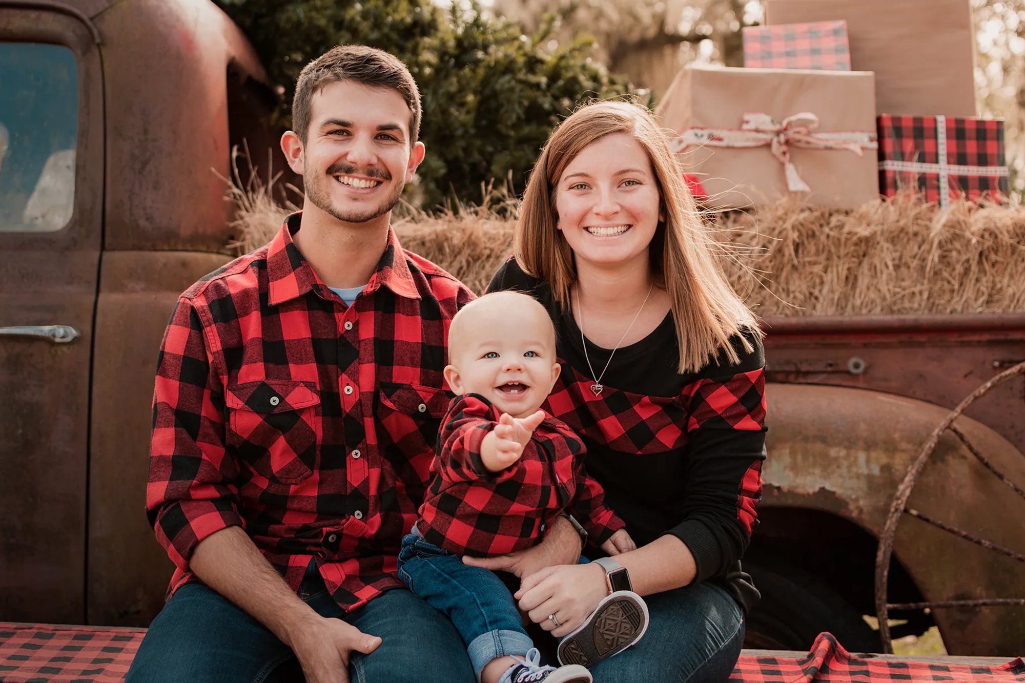 Family in coordinating red-and-black plaid seated beside a vintage truck.