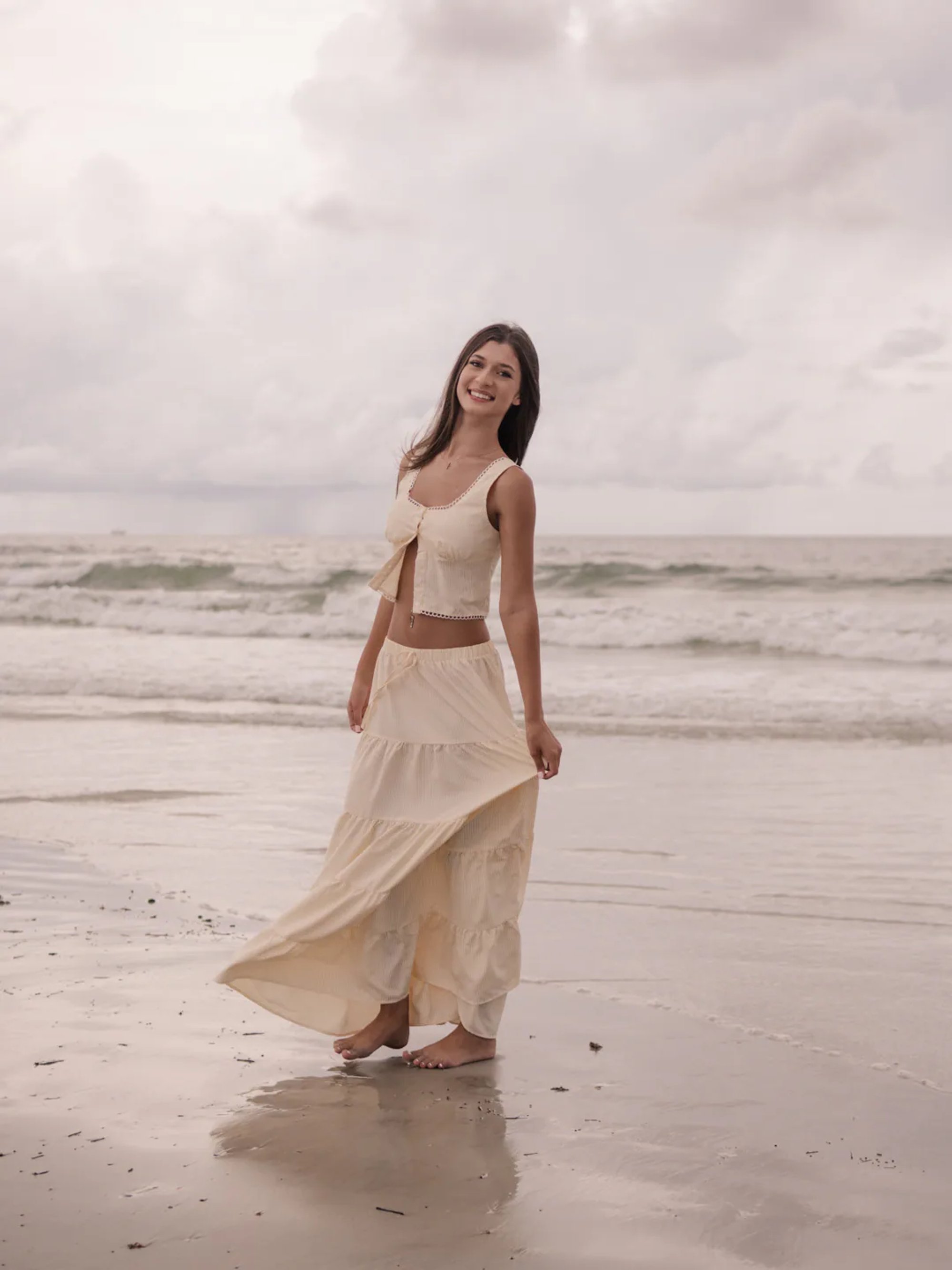 Young woman in a cream outfit standing at the edge of the surf.