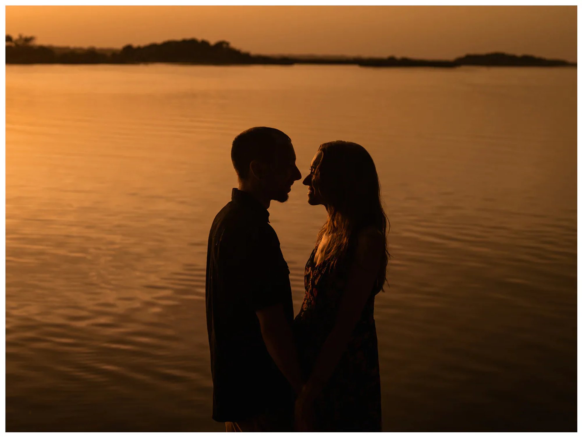 Couple holding hands and facing each other in silhouette beside the river at Washington Oaks Gardens.