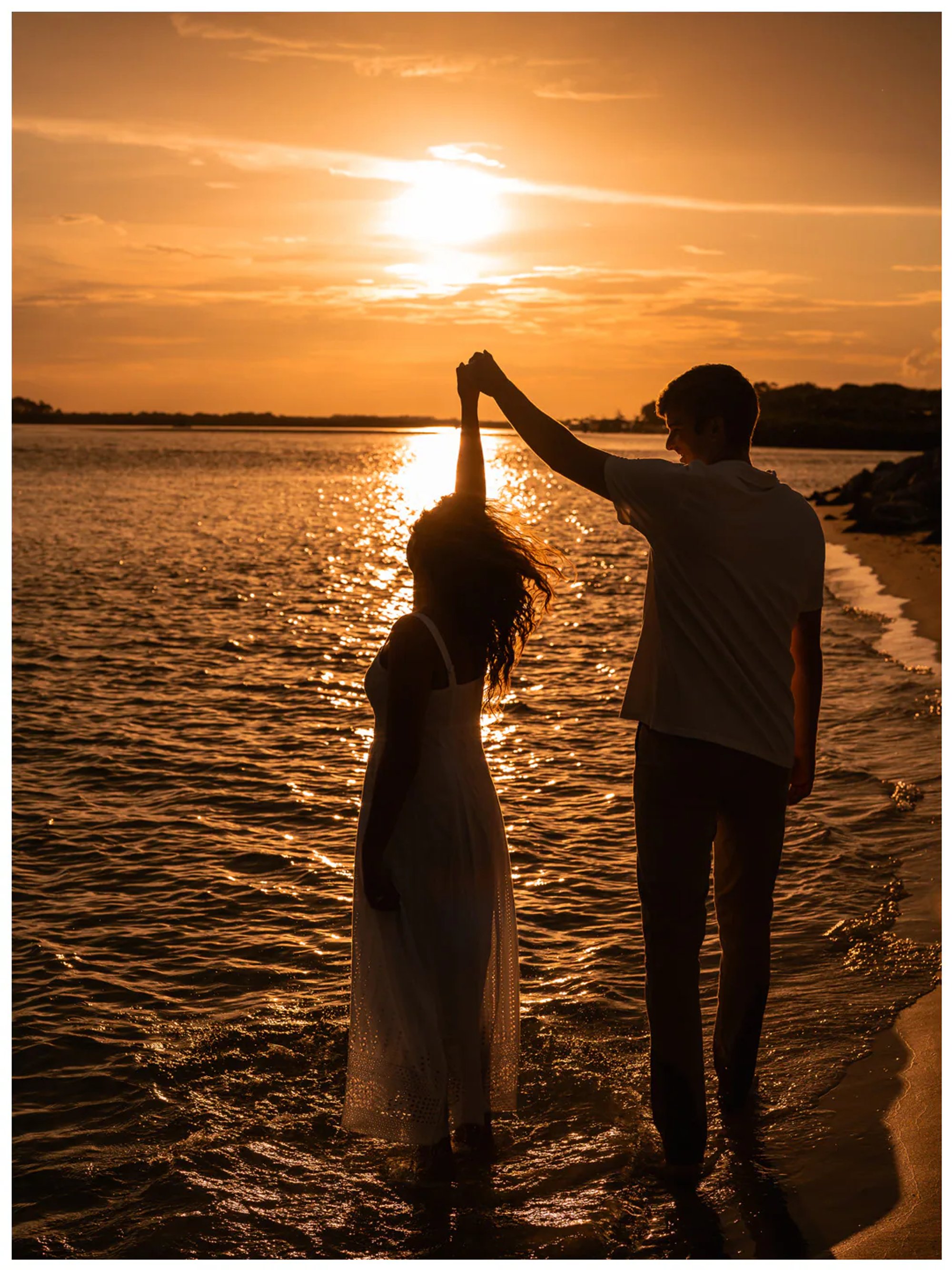 Silhouetted couple dancing beside the water at sunset.
