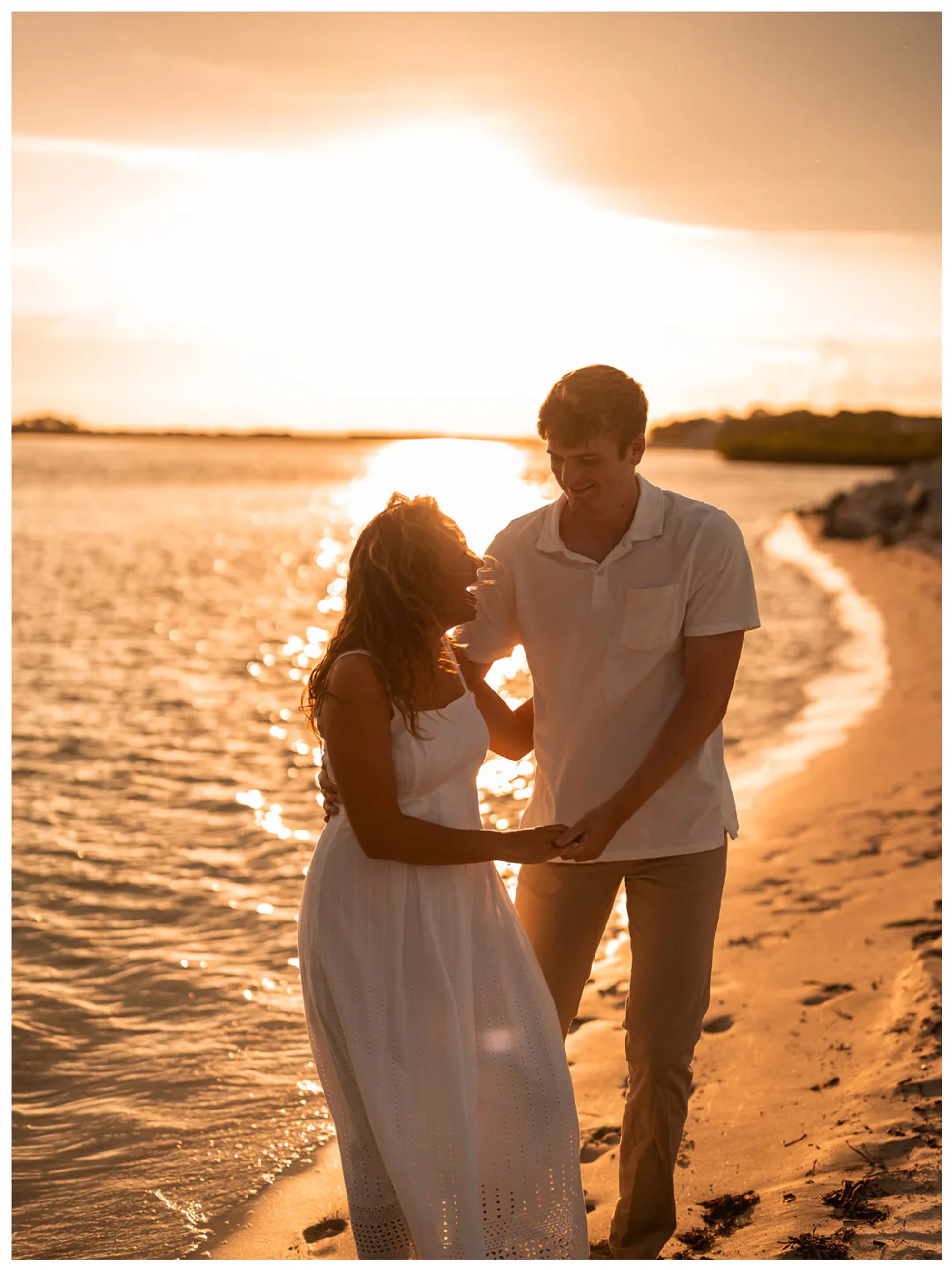 Couple holding hands beside the water at sunset.