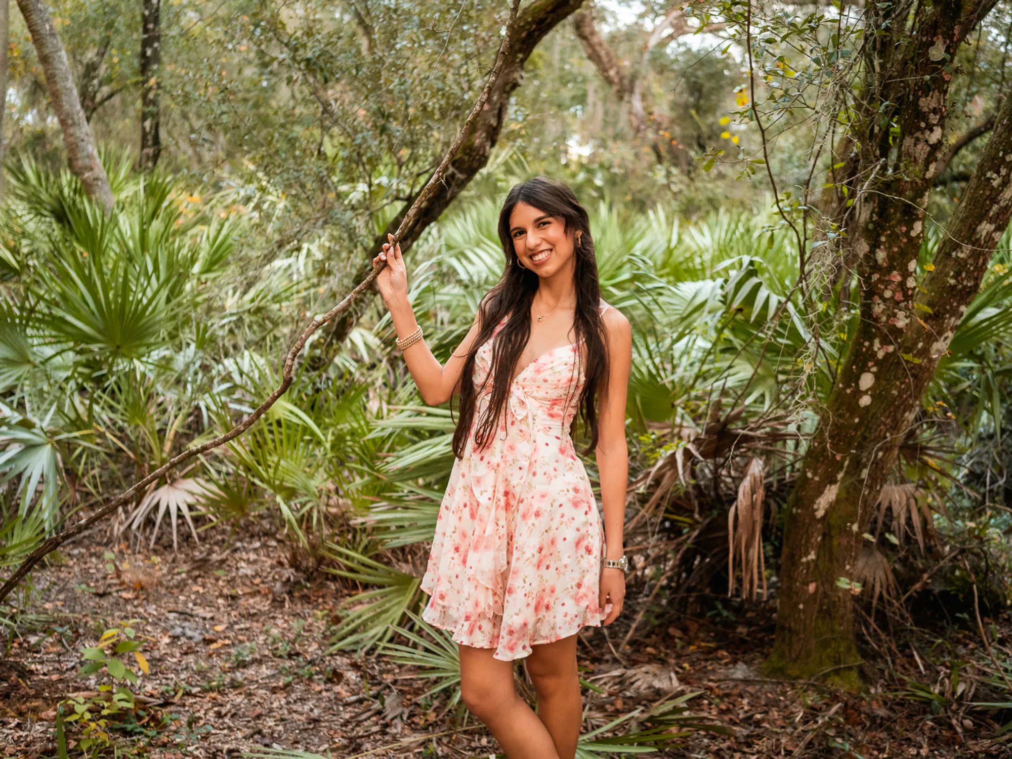 Young woman in a floral dress holding a slender tree trunk.