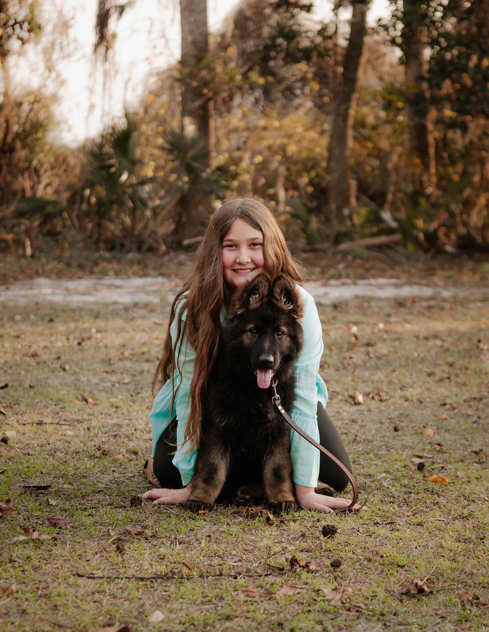 Young woman crouching beside her black dog on the grass.