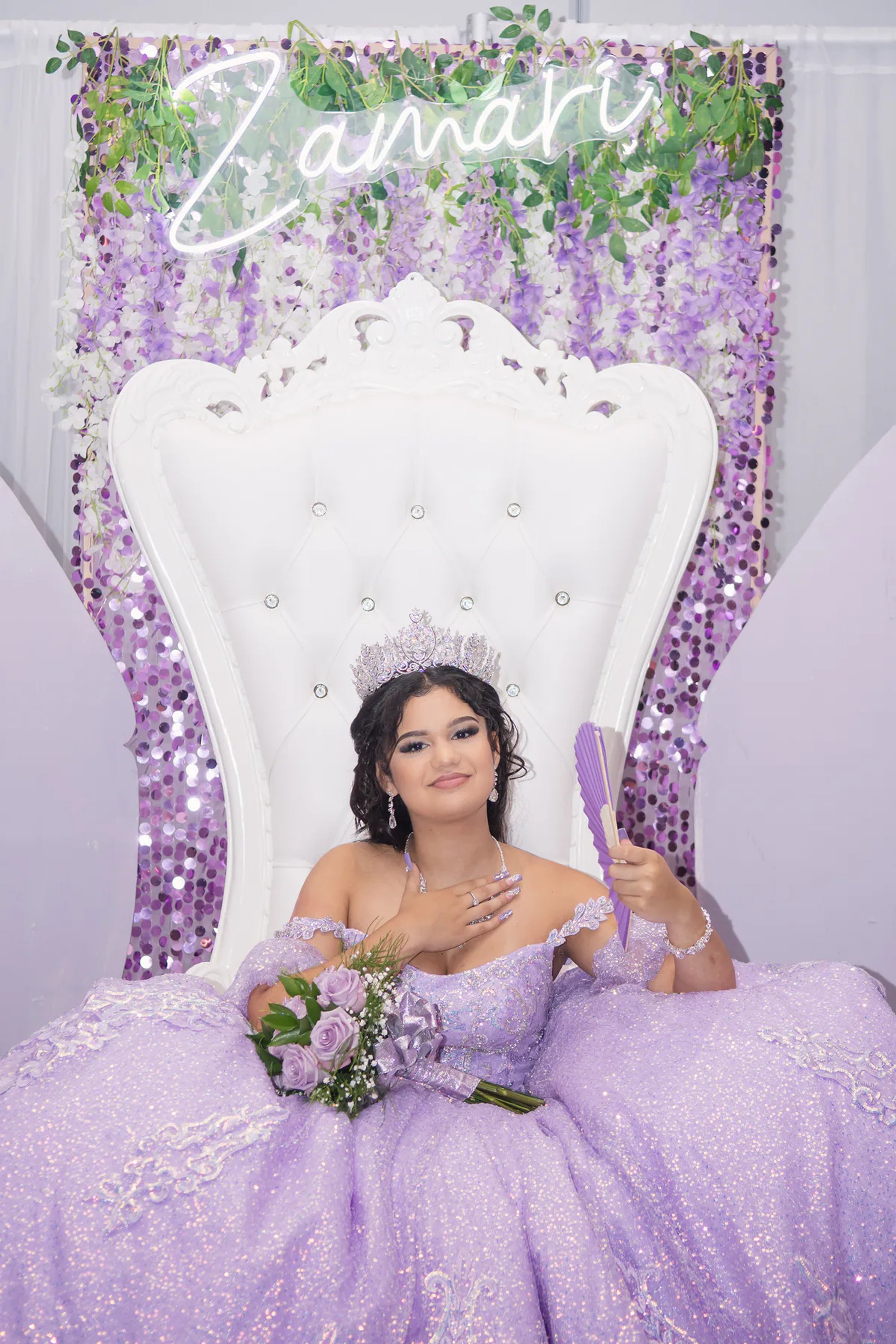 Quinceañera seated on a white throne chair with her purple bouquet.