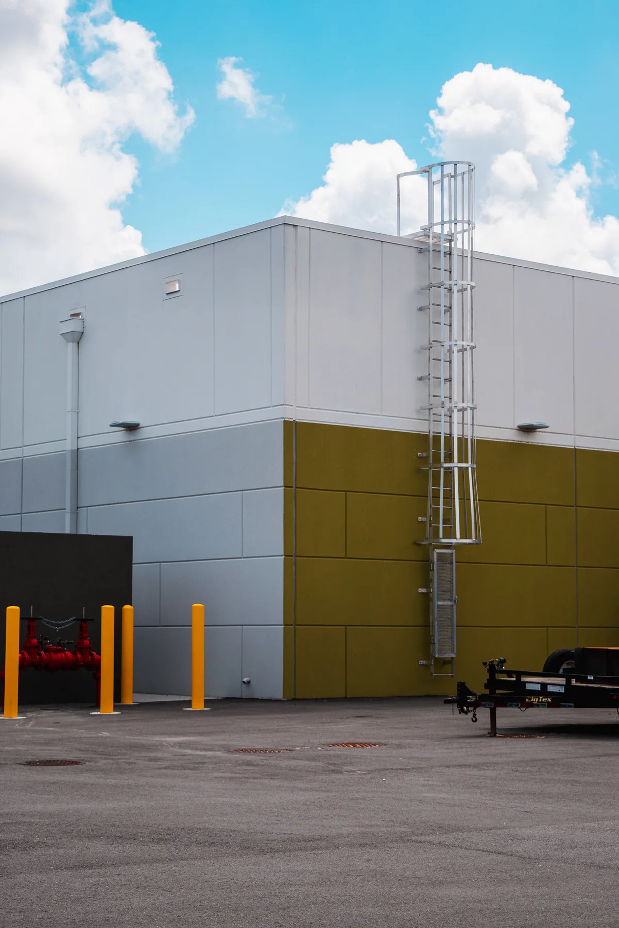 Color-blocked warehouse exterior with a metal ladder and yellow bollards.