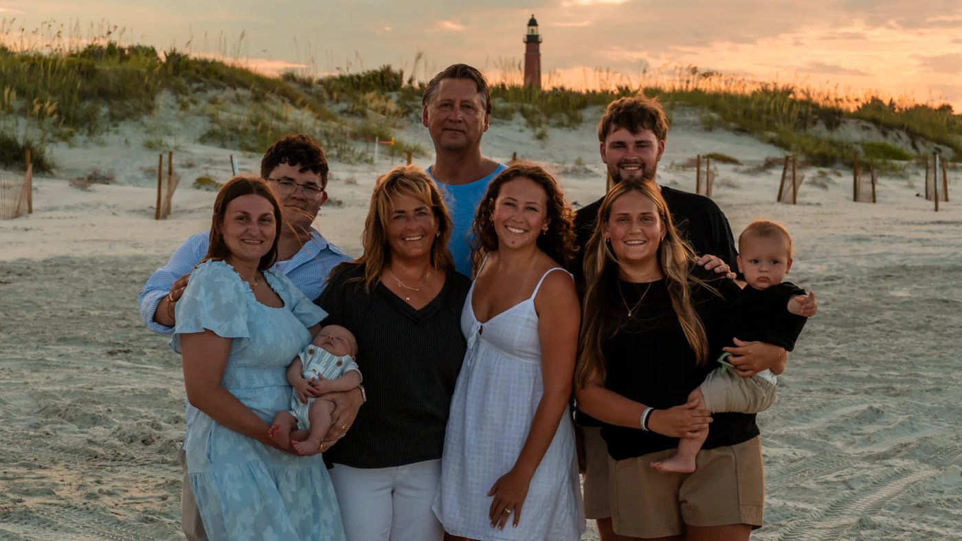 Extended family gathered on the beach with a lighthouse in the distance.