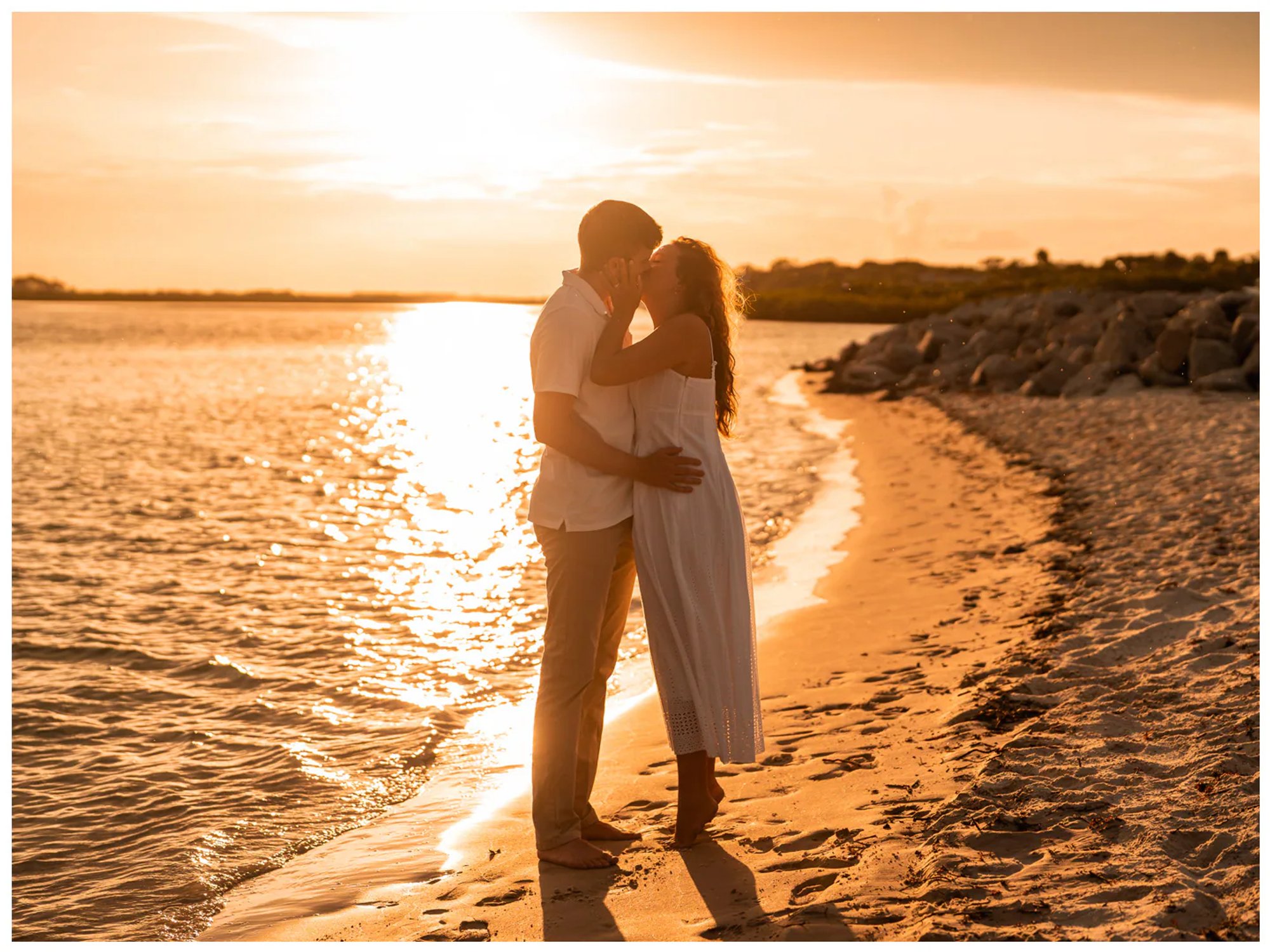 Couple standing together at the edge of the water in golden light.