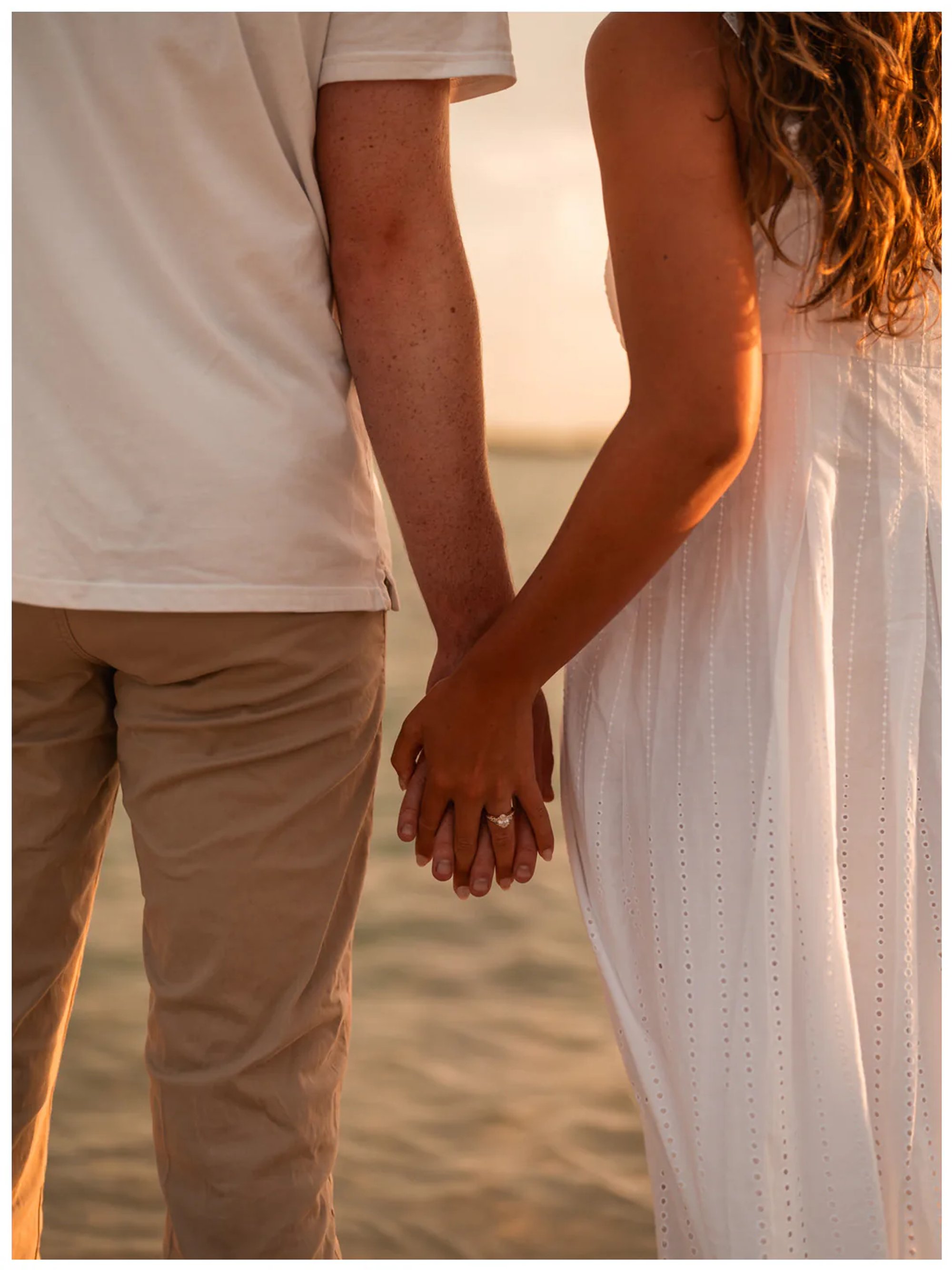 Close view of a couple holding hands in warm sunset light.