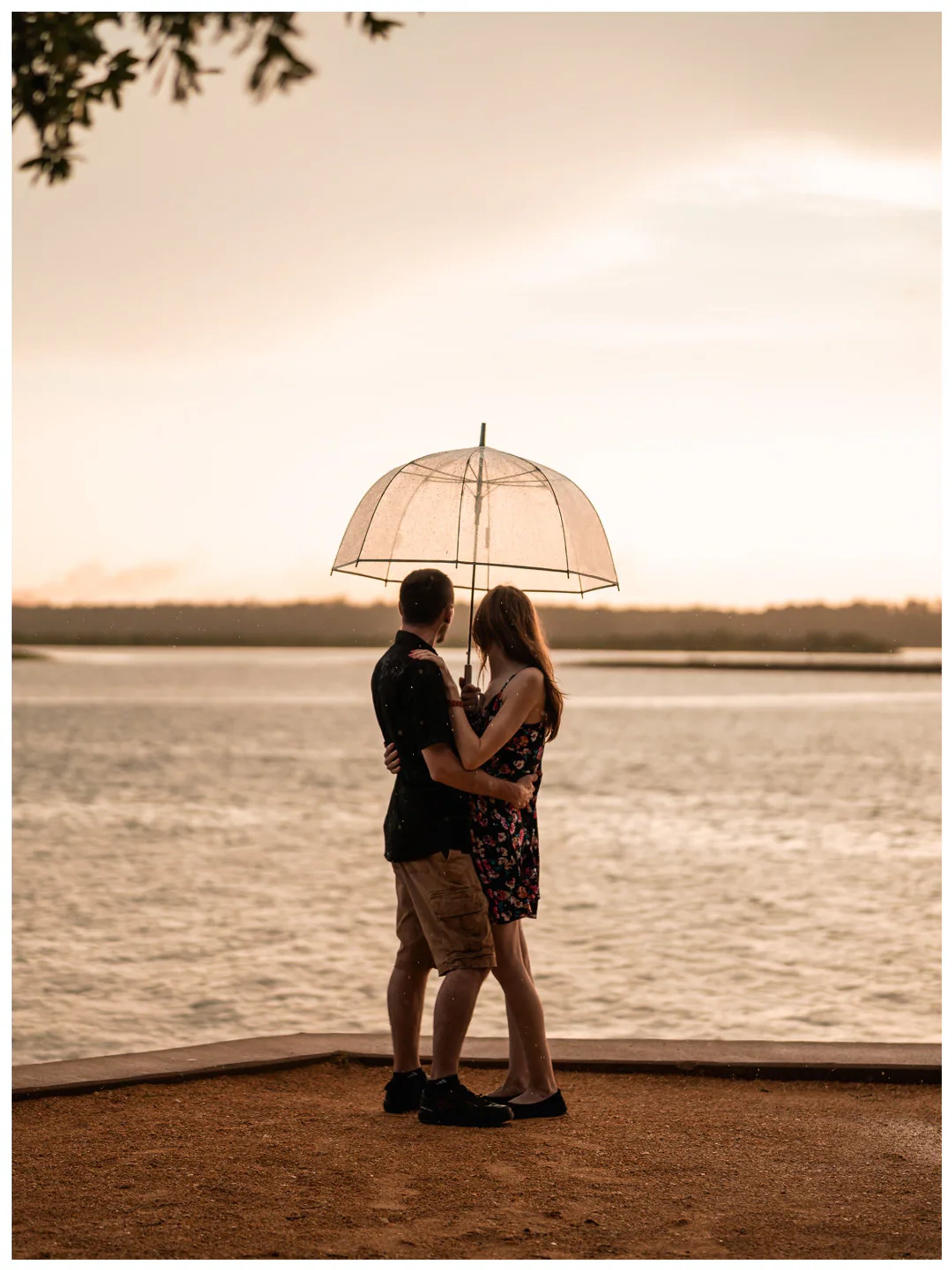 Wide portrait of a couple embracing beneath an umbrella beside the river at Washington Oaks Gardens State Park.