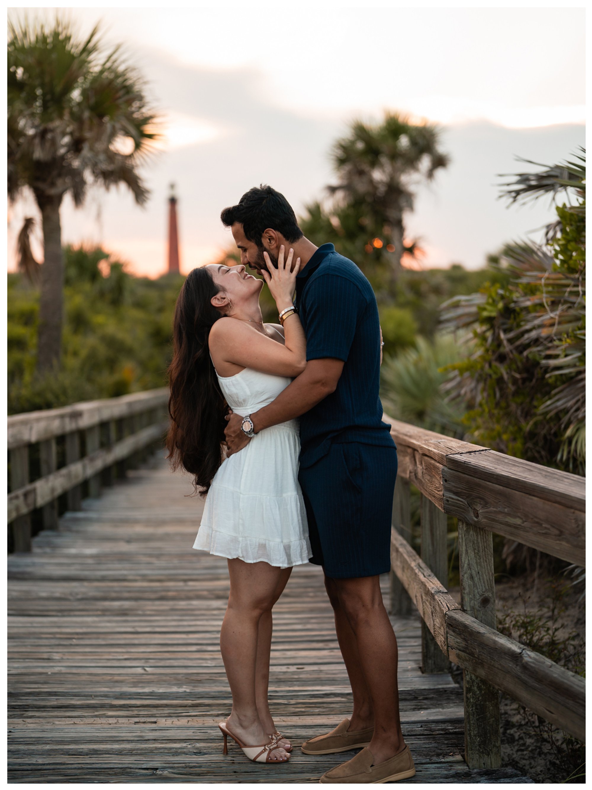 Dierick and Paulina sharing a kiss on the boardwalk with the Ponce Inlet Lighthouse behind them.