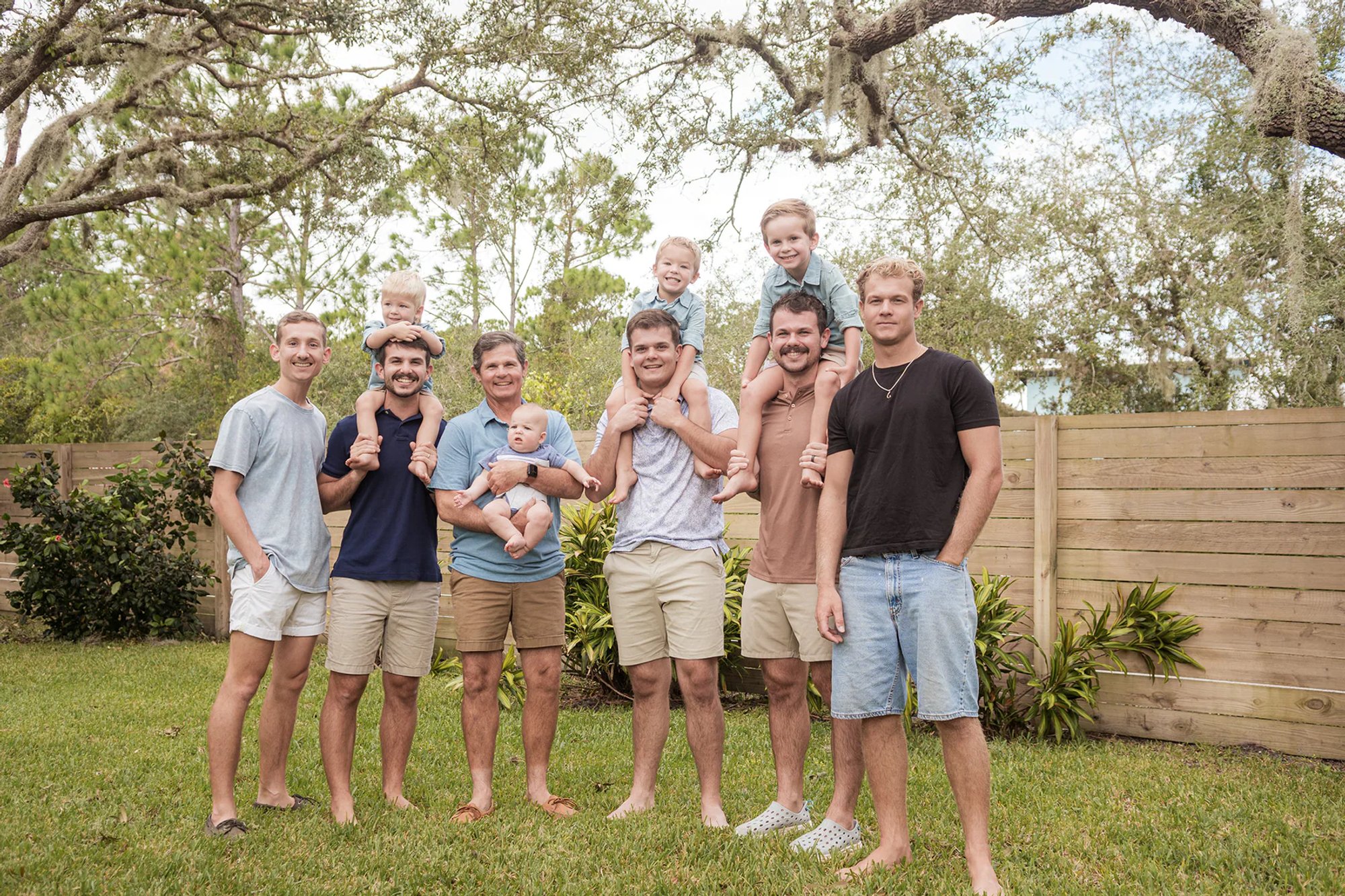 Group of men and young children gathered together beneath a live oak tree.