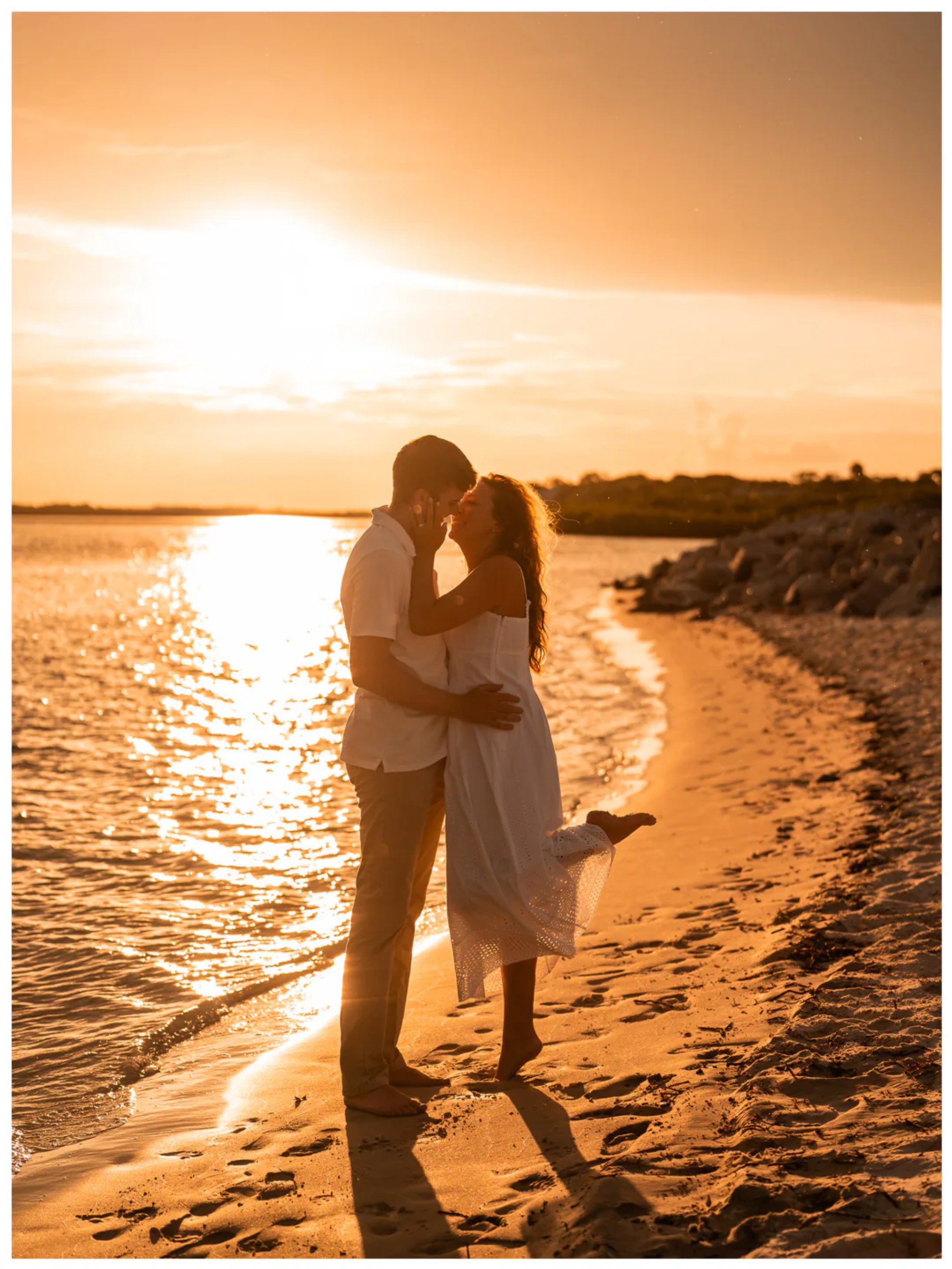 Couple embracing on the shoreline with one partner lifting a leg.