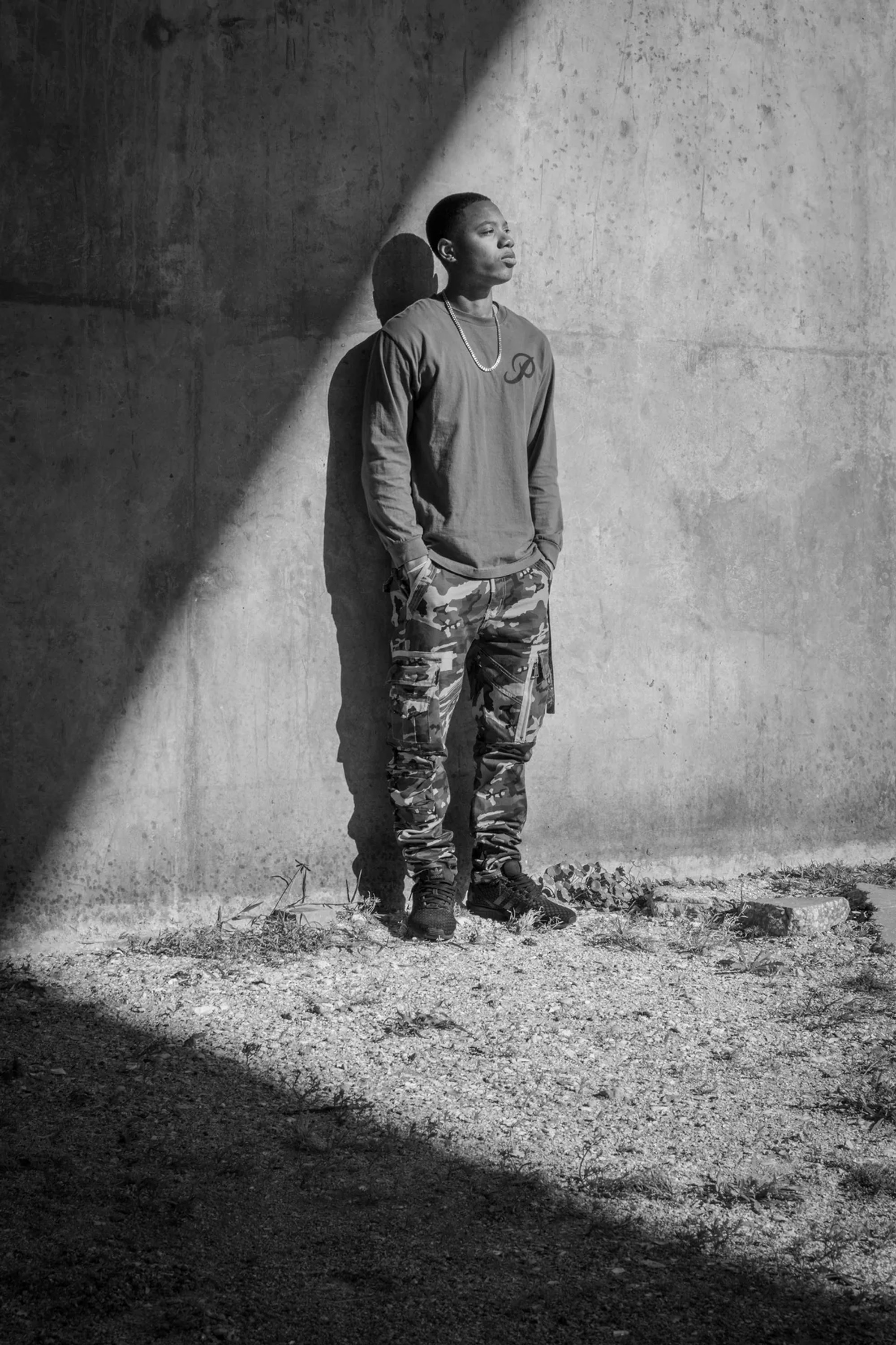 Man facing a concrete wall in a dramatic black-and-white portrait.