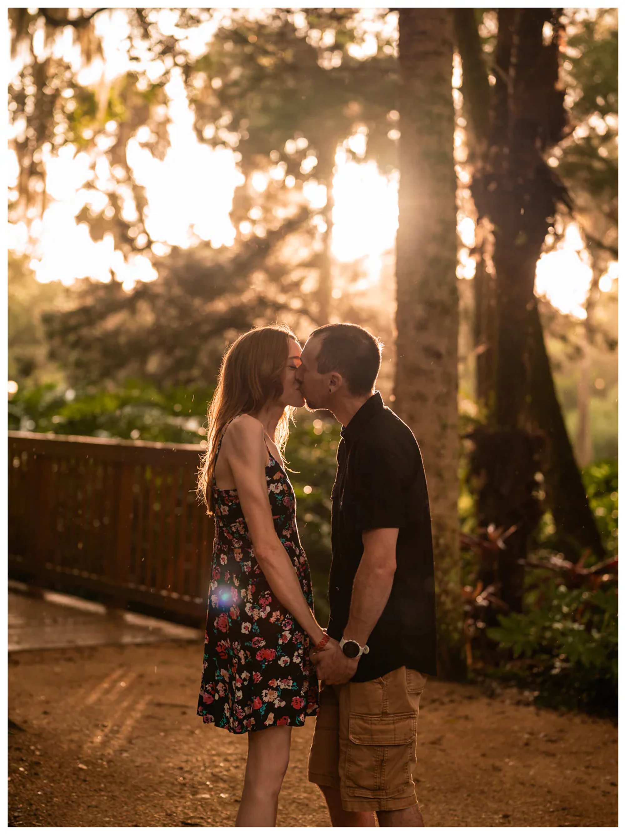 Couple holding hands on a garden path with warm sunlight filtering through the trees at Washington Oaks.