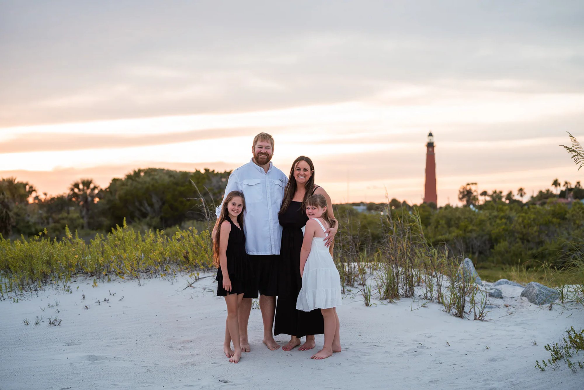 Family standing together on the sand with Ponce Inlet Lighthouse in the background.