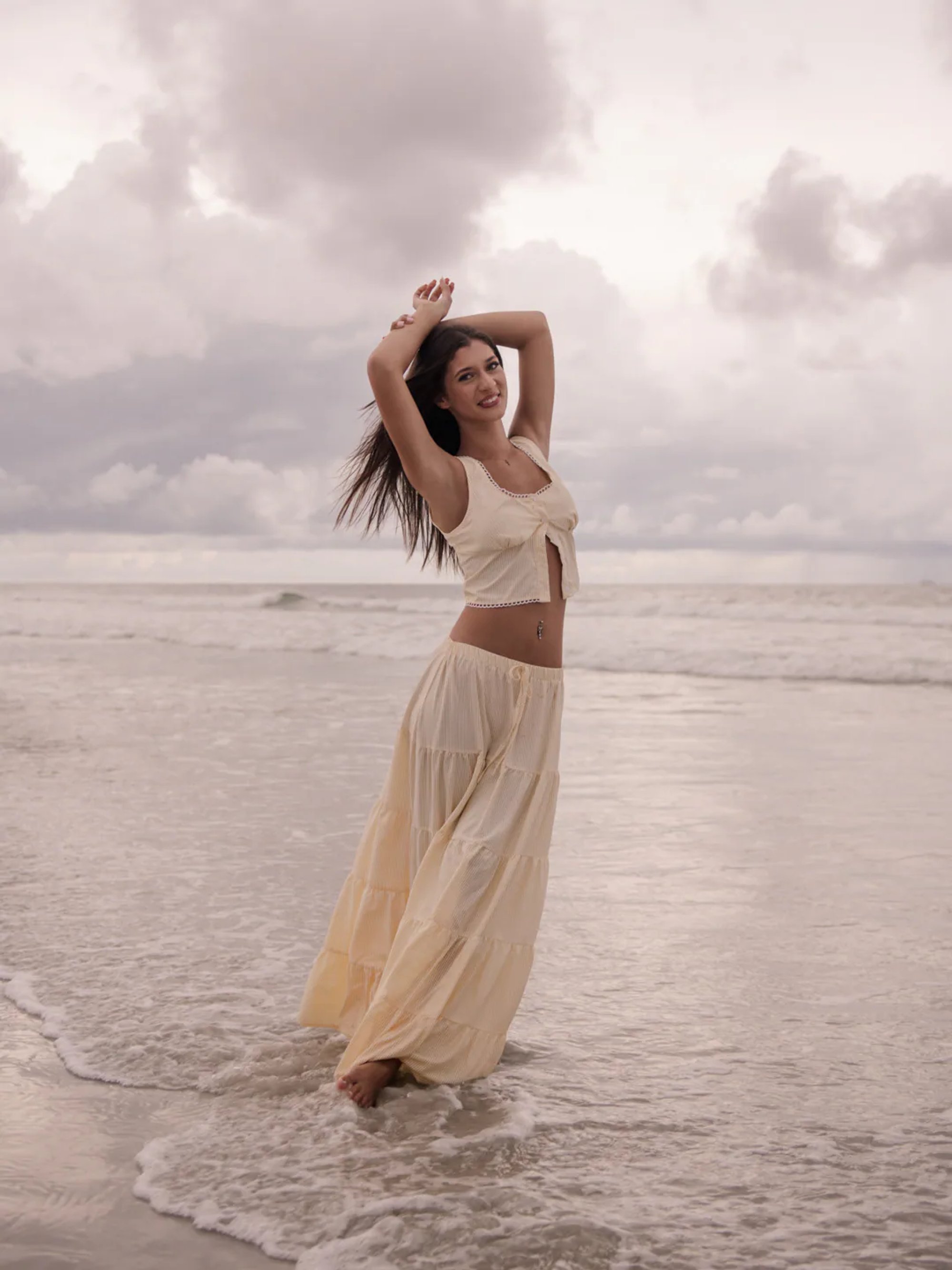 Young woman in a flowing cream outfit standing in shallow ocean water.