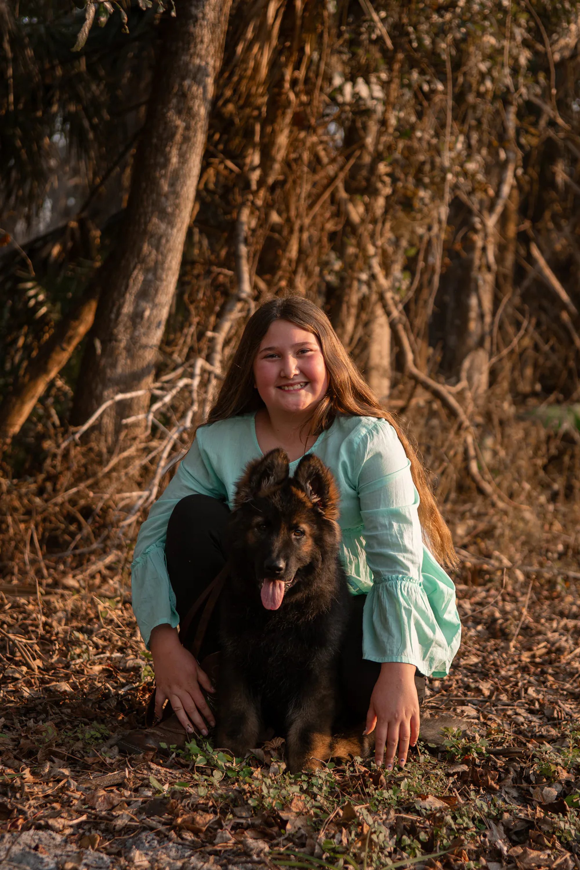 Young woman and her black dog seated beneath large tree roots.