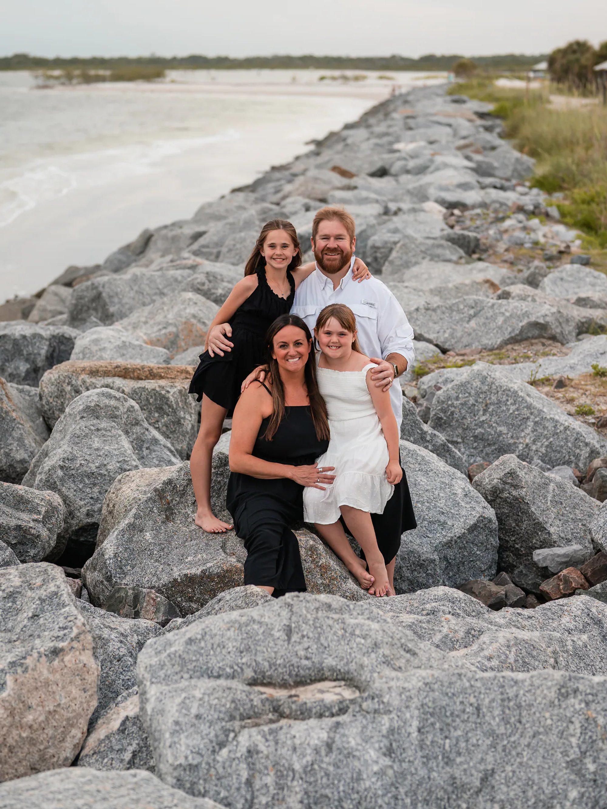 Family sitting together on the rocks during a Ponce Inlet Beach photo session.