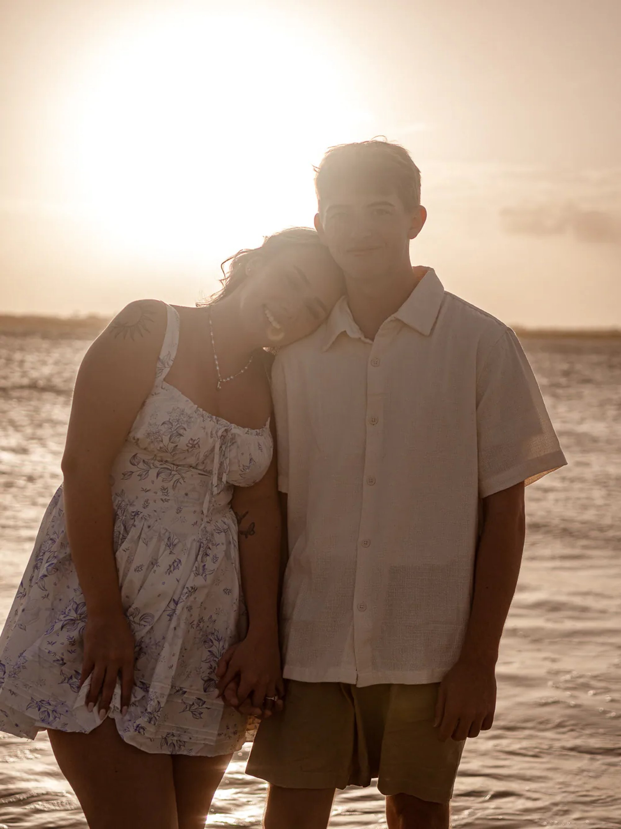Backlit couple standing together beside the ocean.