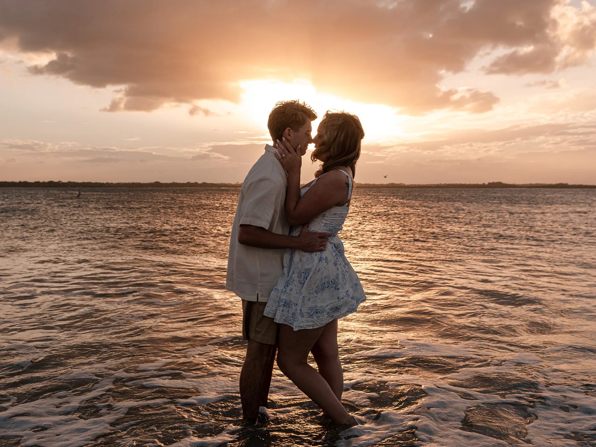 Couple kissing in shallow ocean water at sunset.