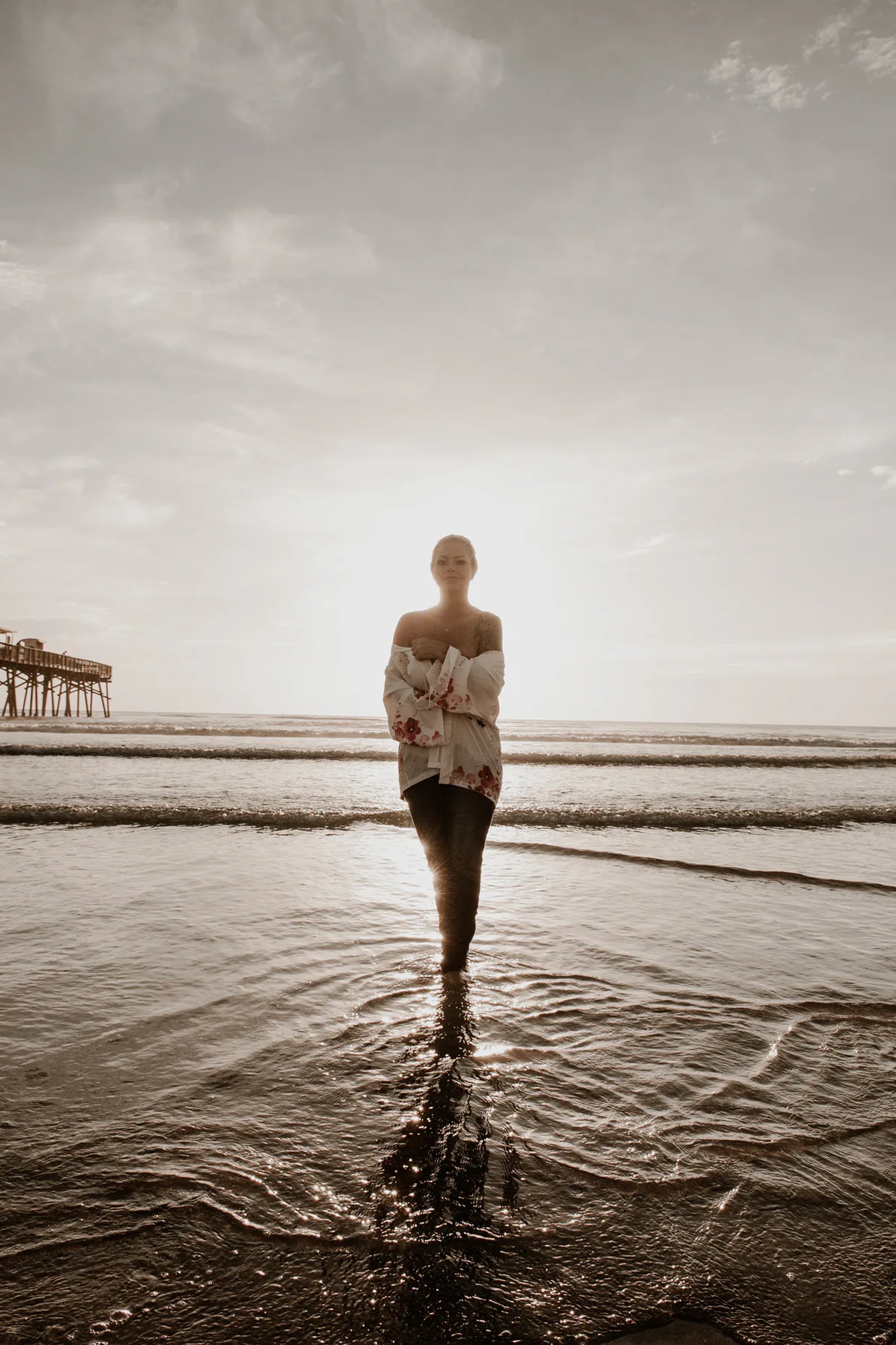 Backlit woman standing in shallow water with the ocean horizon behind her.