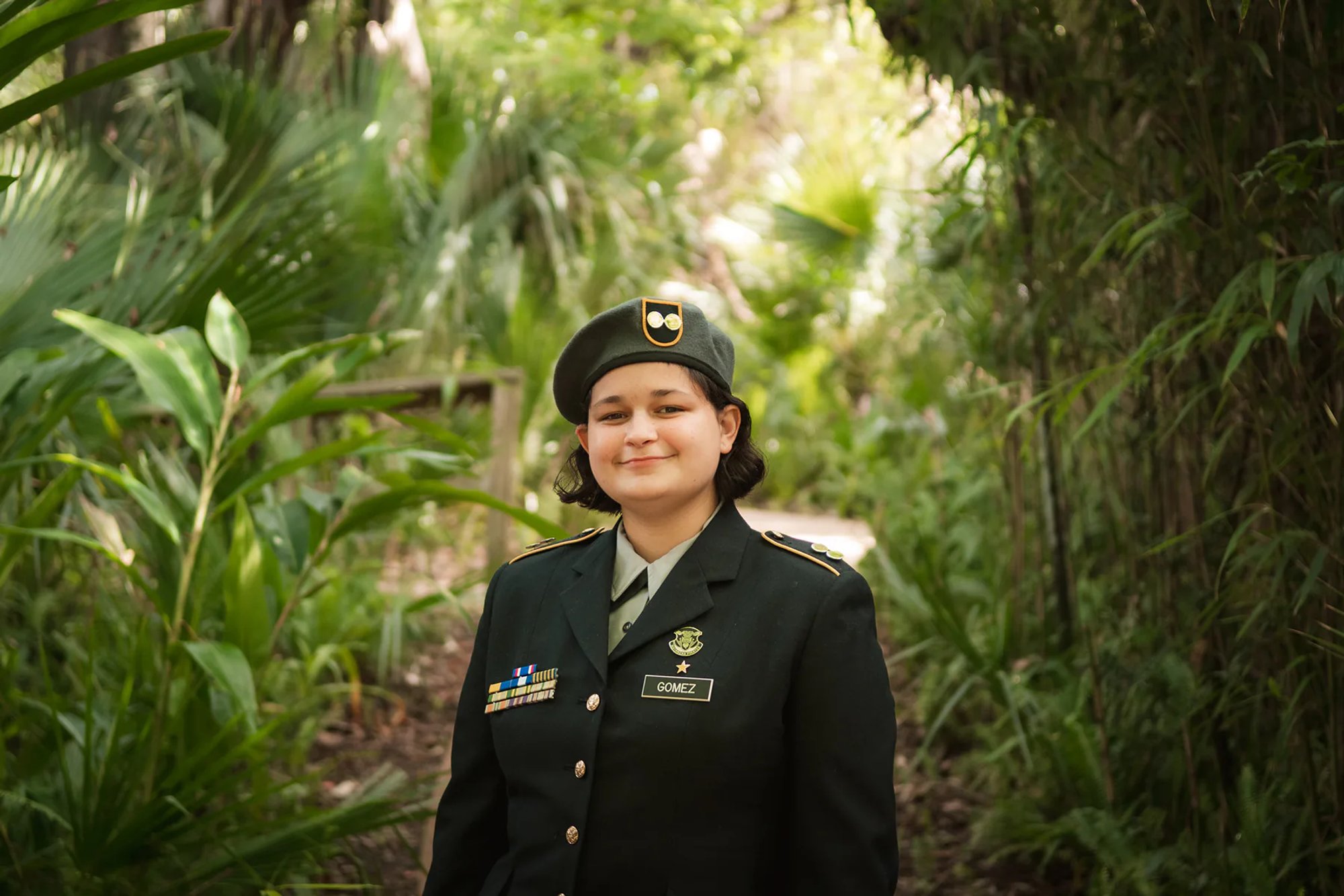 Young person in a decorated dress uniform standing among tropical greenery.