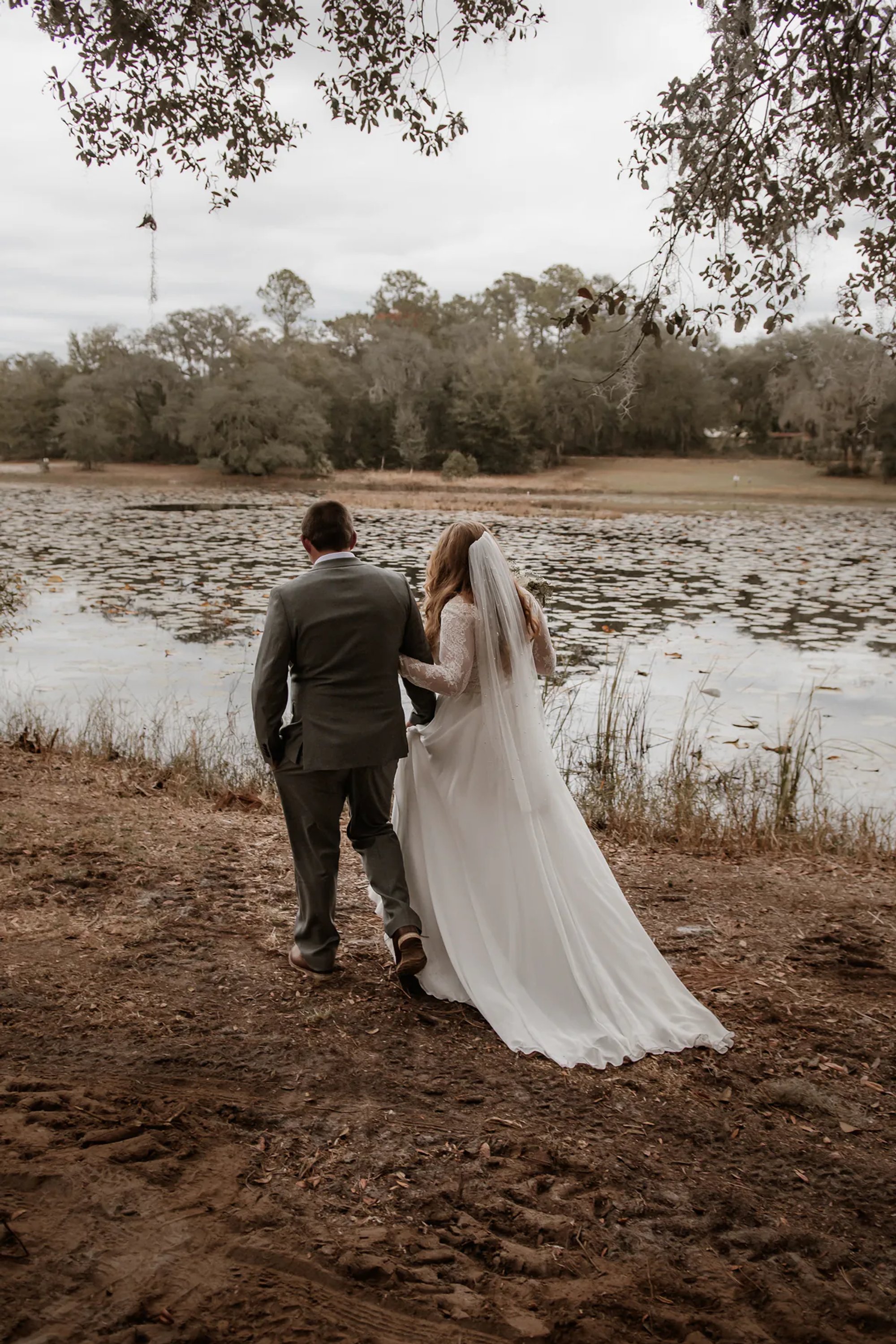 Bride and groom walking hand in hand beside a pond.