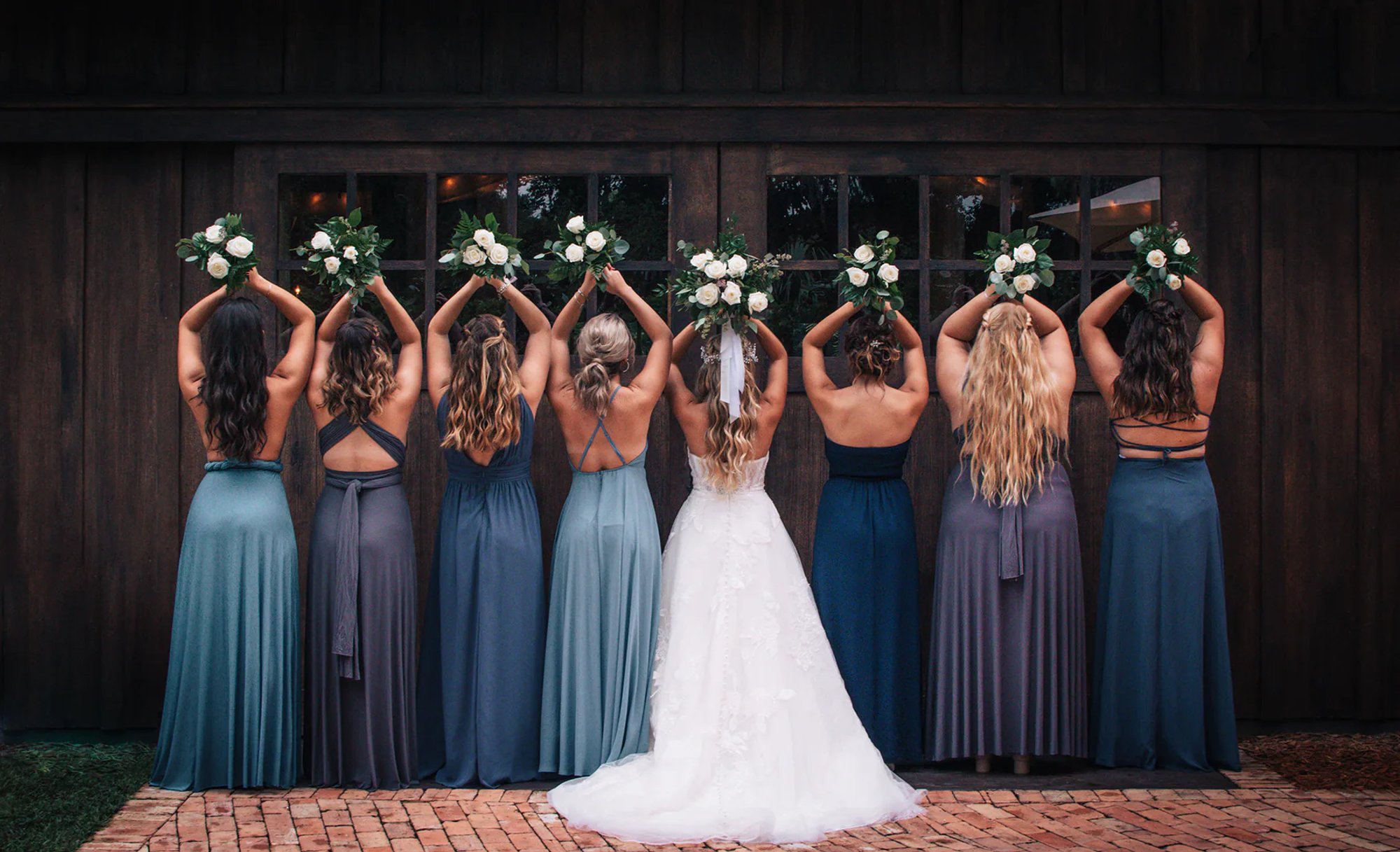 Bride and bridesmaids raising their bouquets with their backs to the camera.