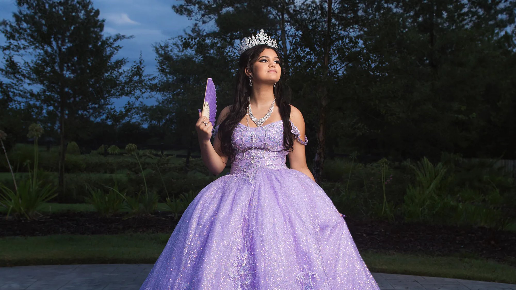 Quinceañera in a sparkling purple gown holding a folding fan.