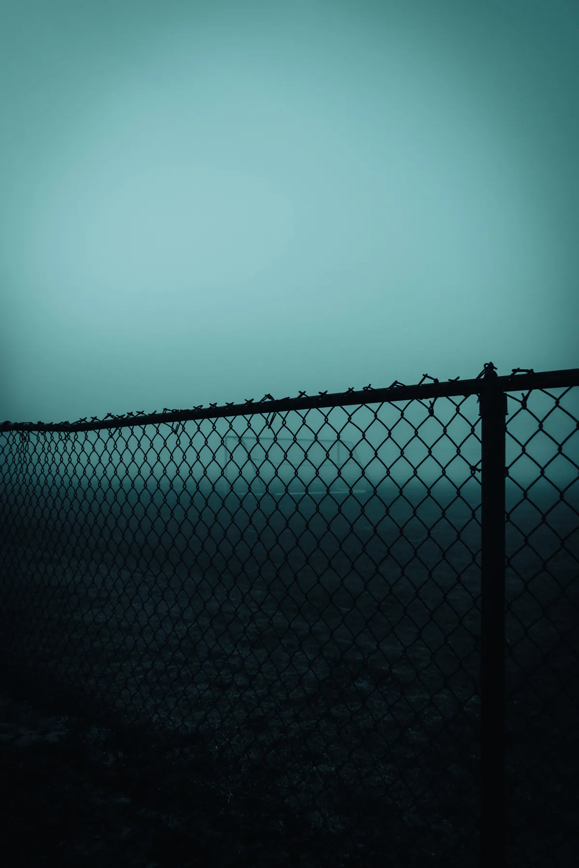 Chain-link fence silhouetted against a misty blue sky.