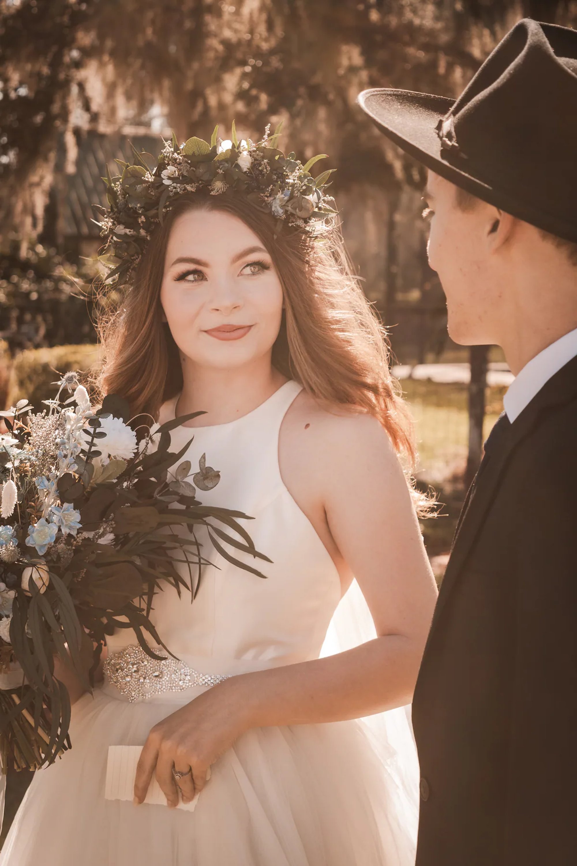 Sunlit bride holding a bouquet while looking toward the groom.