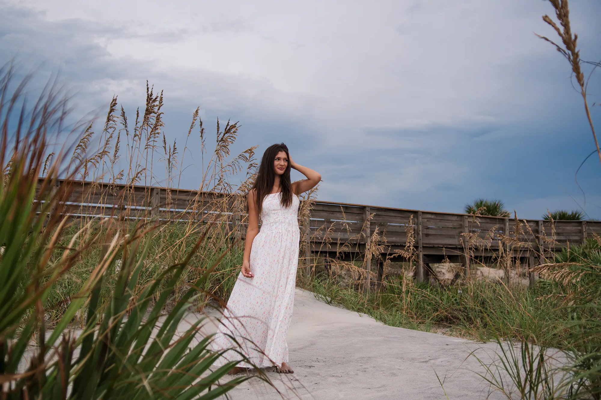 Senior photos in Port Orange FL area, Mia in a floral maxi dress standing near sea oats at Ponce Inlet.