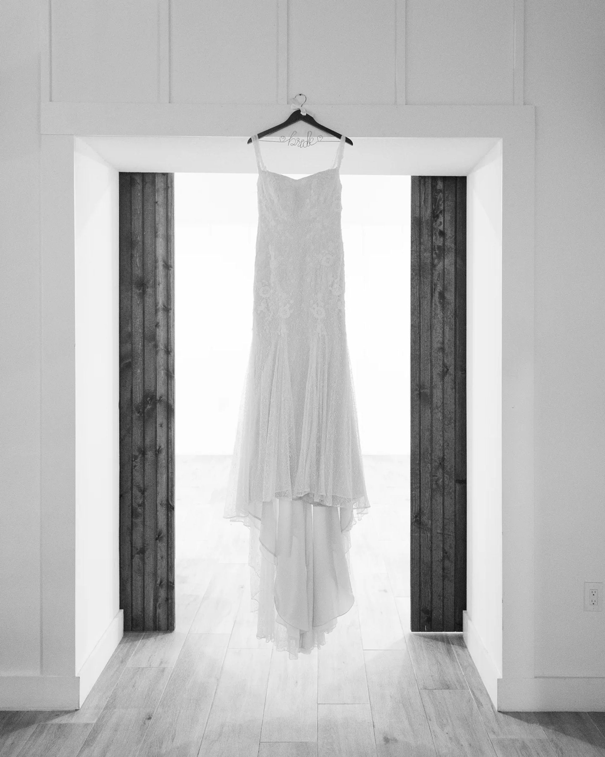 Wedding dress hanging in a bright doorway in black and white.