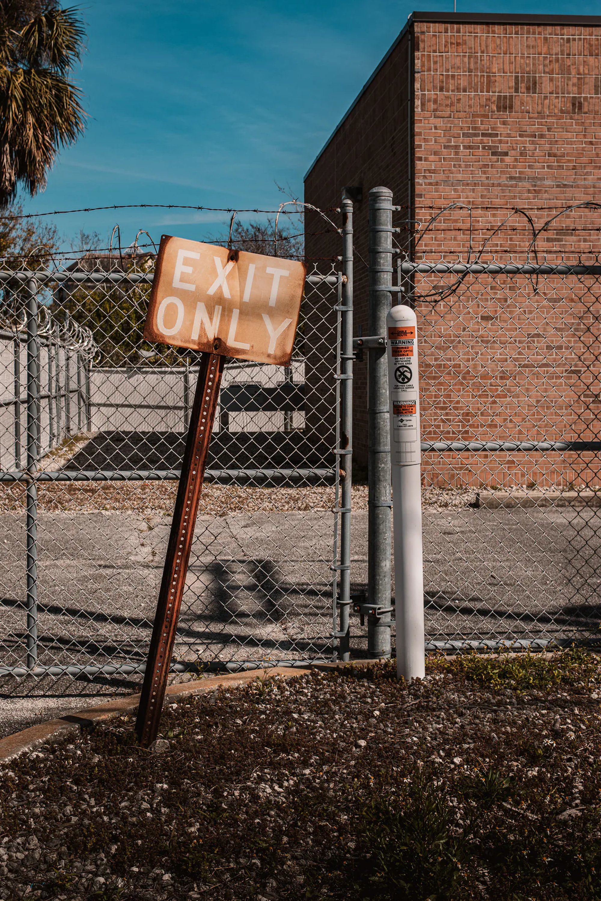 Exit-only sign beside a chain-link fence and brick industrial buildings.