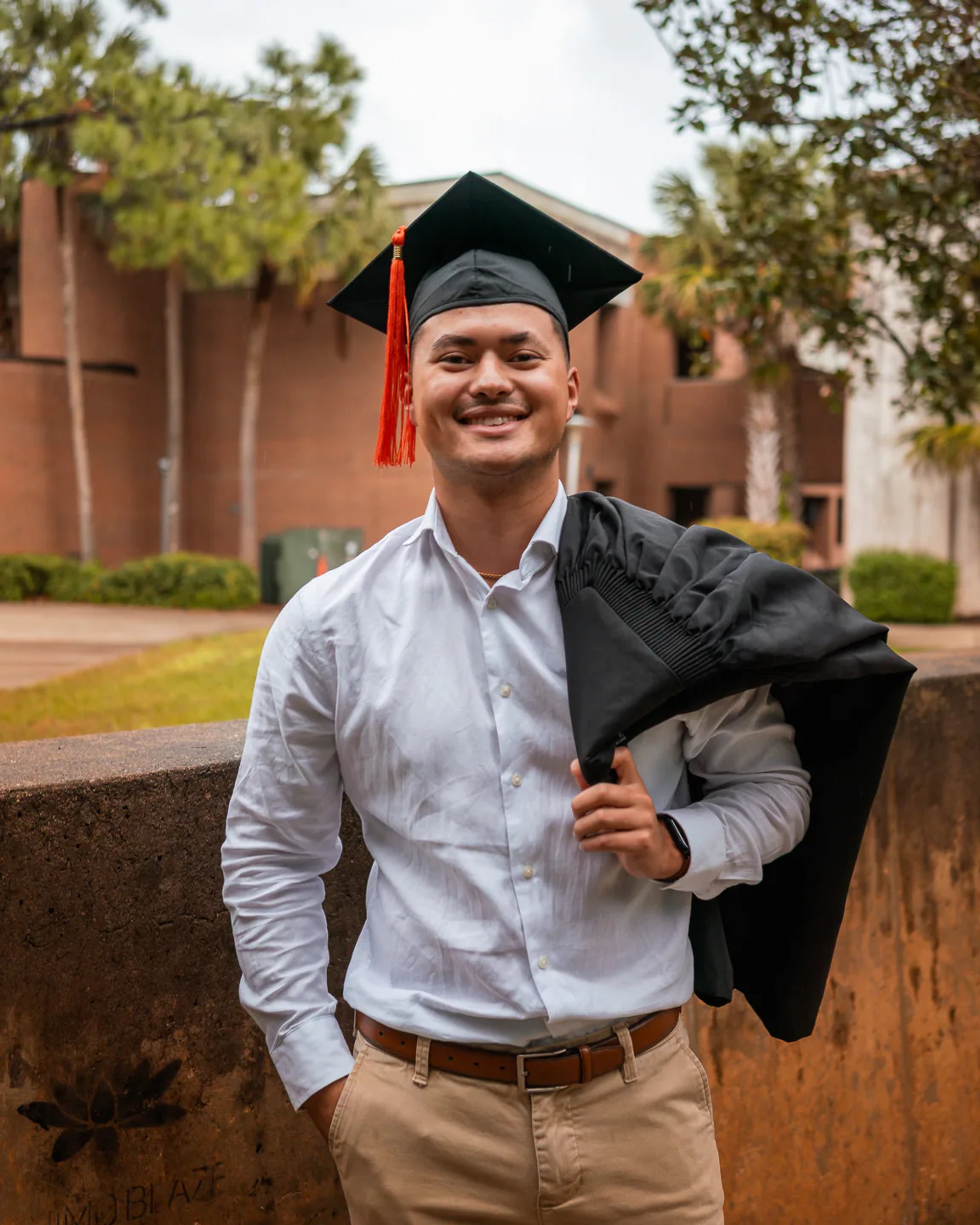 Smiling male graduate holding his black gown over one shoulder.