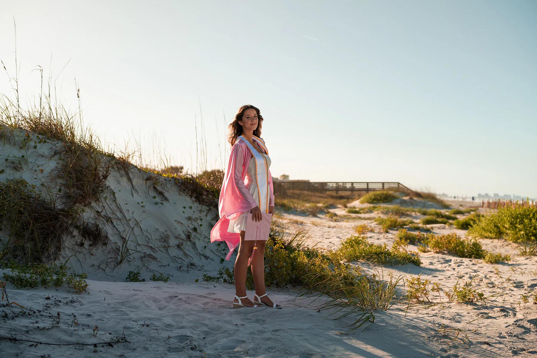 Young woman wearing a pink wrap over a white dress among coastal dunes.