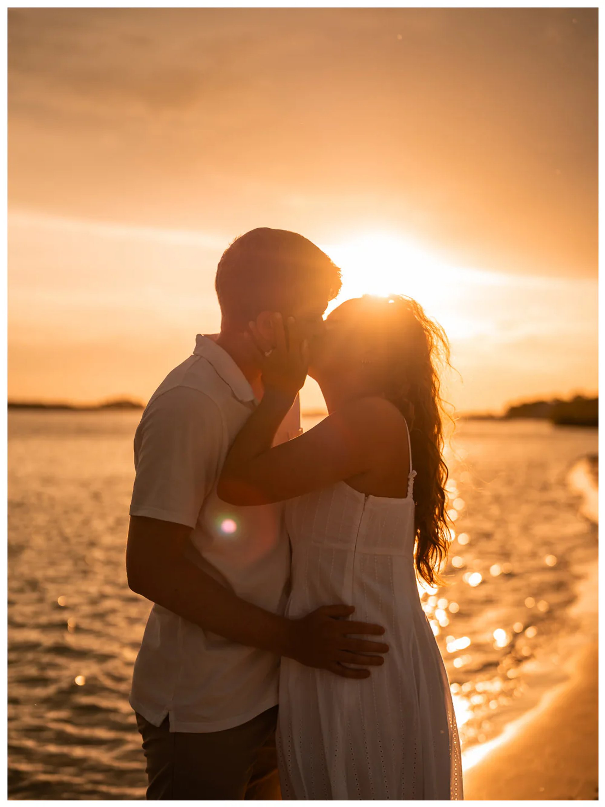 Backlit couple kissing at the edge of the water.